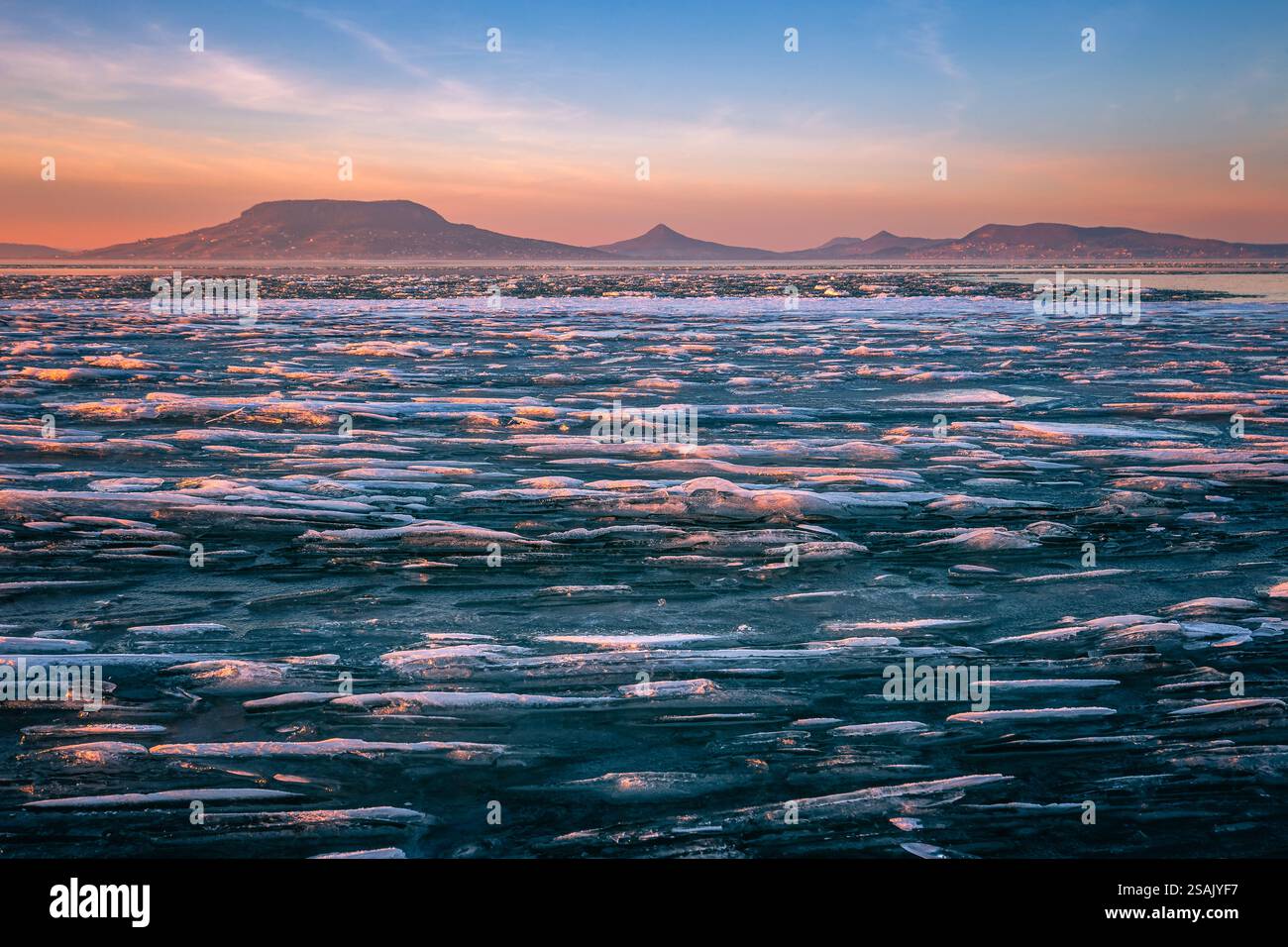 Fonyod, Hongrie - vue panoramique sur le lac Balaton gelé par un après-midi froid d'hiver avec des lumières dorées de coucher de soleil et la montagne Badacsony en arrière-plan Banque D'Images
