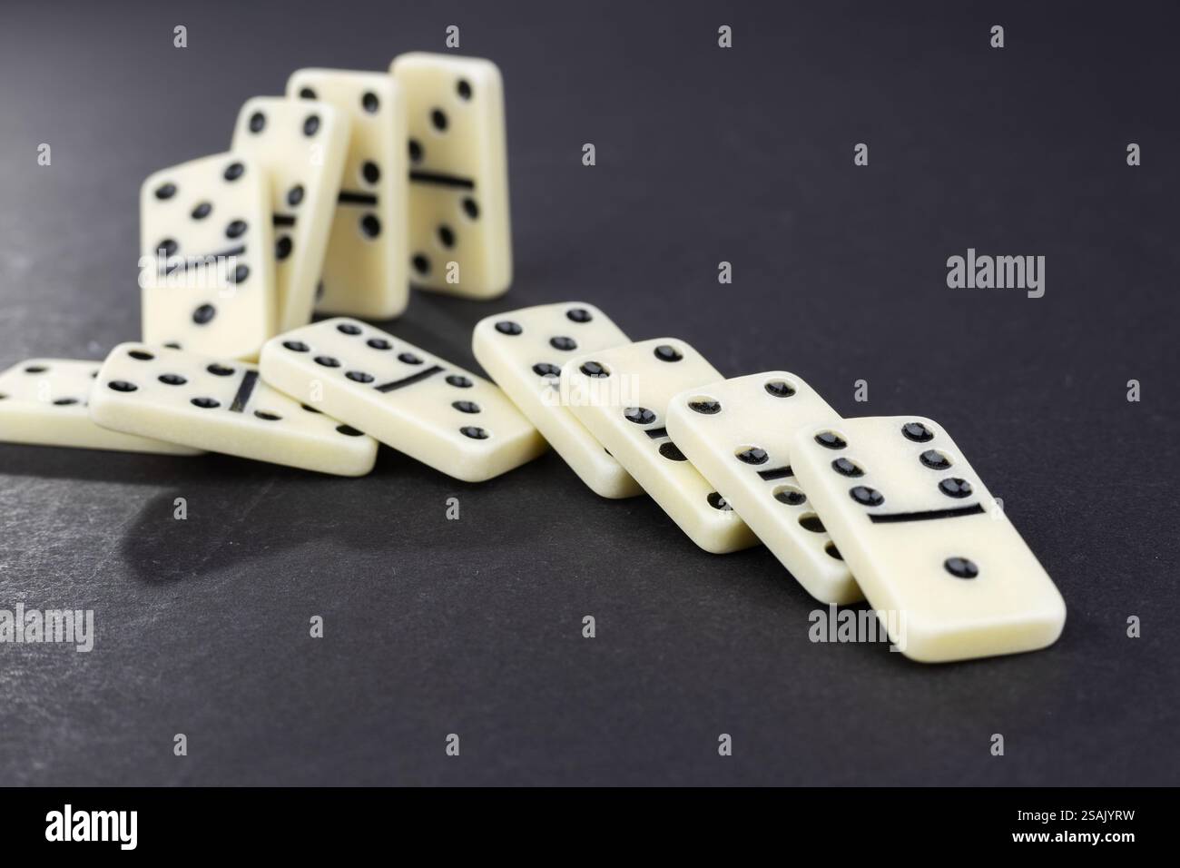 Concept d'effet Domino avec des pièces de dominos blanc rangée tombant sur fond sombre. Gestion des crises commerciales, intervention financière, prévention des conflits Banque D'Images