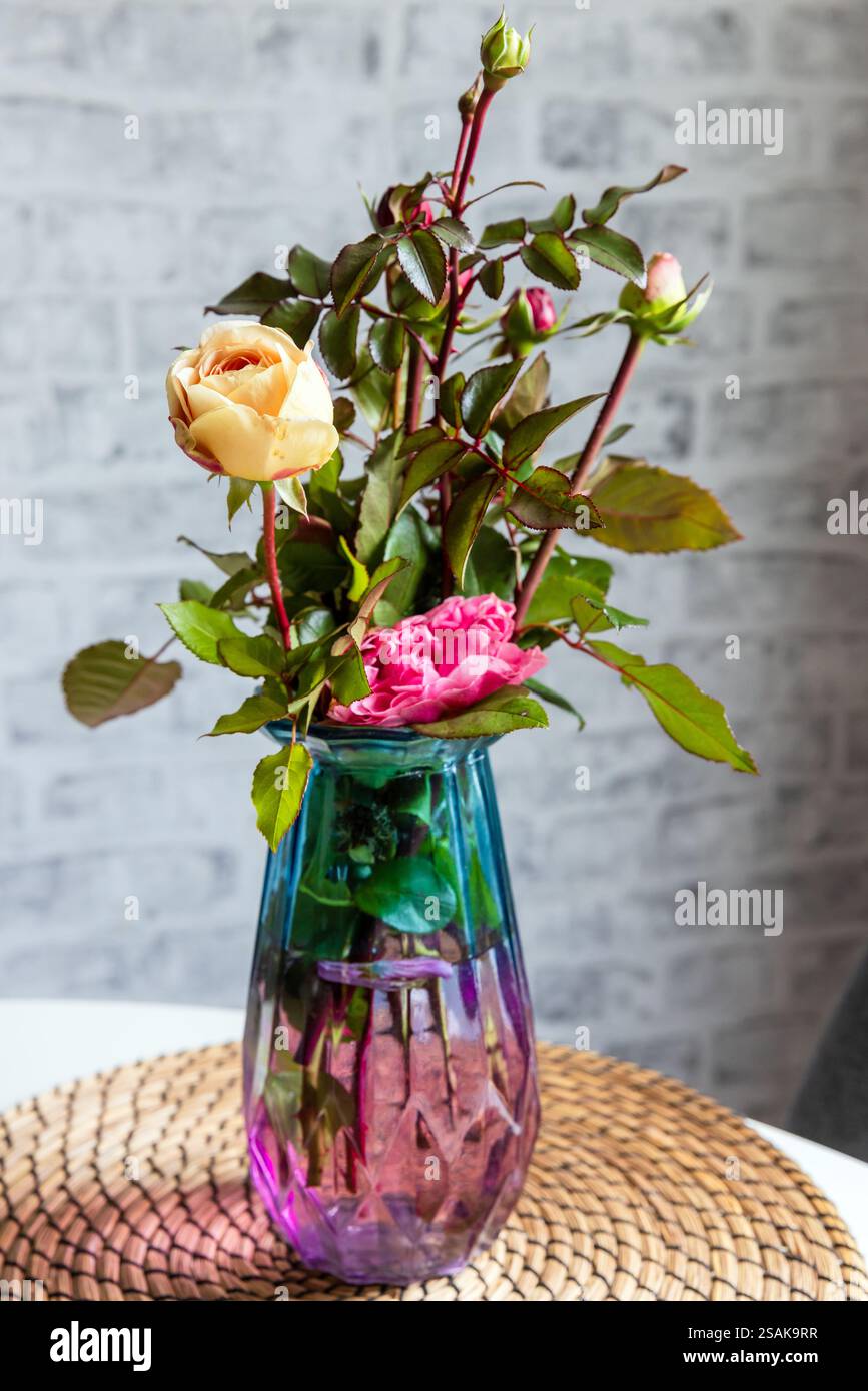Bouquet de roses colorées se tient dans un vase en verre sur fond de mur de briques grises, photo verticale Banque D'Images Bouquet de roses colorées se tient dans un vase en verre sur fond de mur de briques grises, photo verticale Banque D'Images