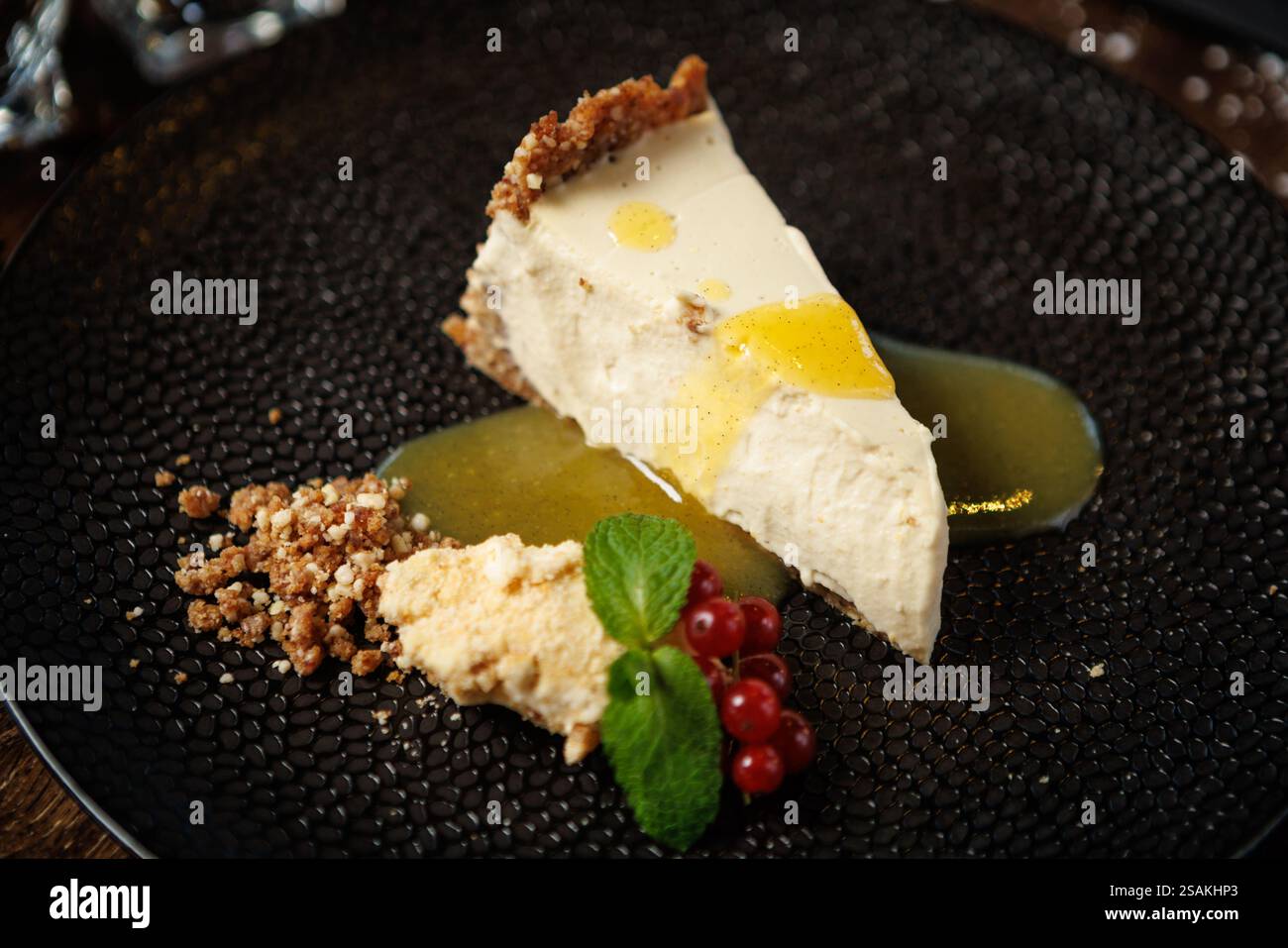 Tranche de cheesecake crémeux avec une croûte de craquelins graham, garnie d'un filet de sauce citron. Garni de feuilles de menthe fraîche, de groseilles rouges et d'un crumble Banque D'Images