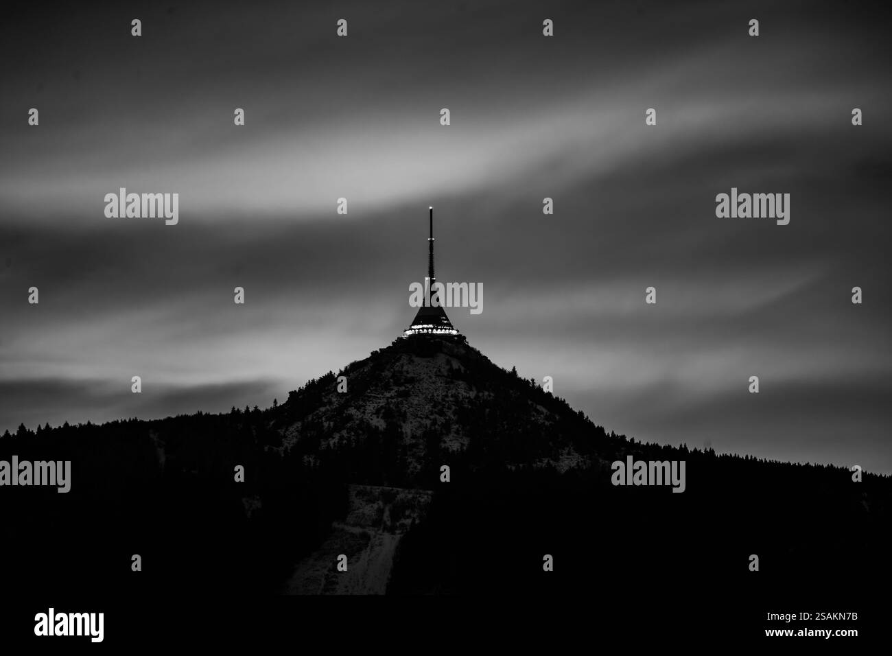 Jested Mountain se dresse majestueusement contre un ciel nocturne hivernal en Tchéquie. La tour à son sommet est illuminée, contrastant avec le paysage sombre et les nuages. Photographie noir et blanc Banque D'Images