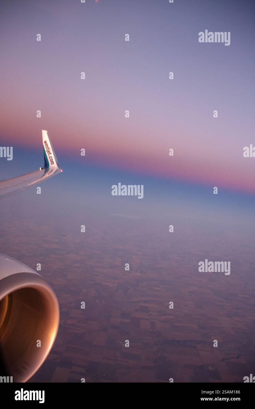 Un avion vole à travers un beau coucher de soleil. Le ciel est rempli d'un mélange de couleurs, y compris des nuances de rose, d'orange et de violet. L'aile de l'avion i Banque D'Images