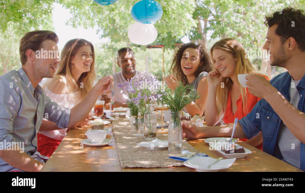 Groupe de jeunes amis multiculturels assis à l'extérieur à table dégustant un gâteau et une boisson chaude ensemble Banque D'Images