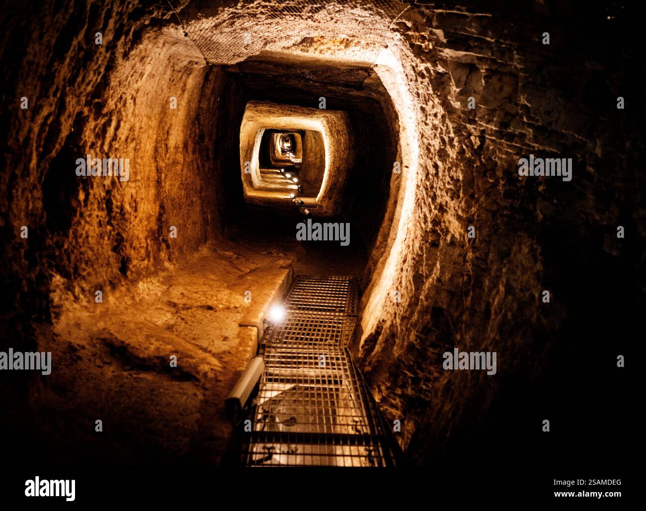 Le tunnel d'Eupalinos avec des murs en pierre brute, avec un chemin sinueux et une grille métallique sur le sol. Le tunnel s'étend au loin, Banque D'Images