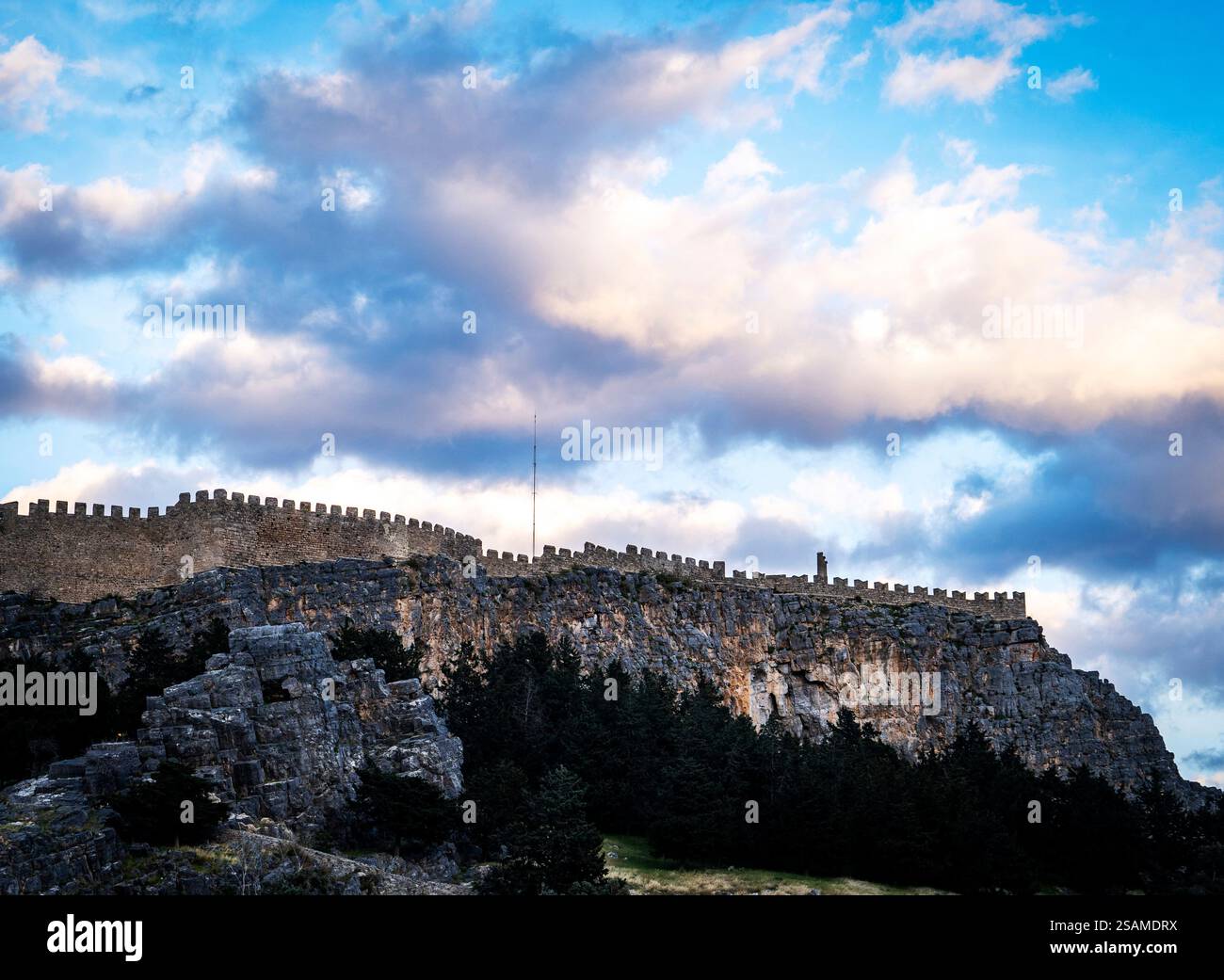Un château historique perché sur une falaise rocheuse, entouré de verdure luxuriante et de nuages spectaculaires dans le ciel. Les murs de pierre sont bien conservés, mettant en valeur Banque D'Images