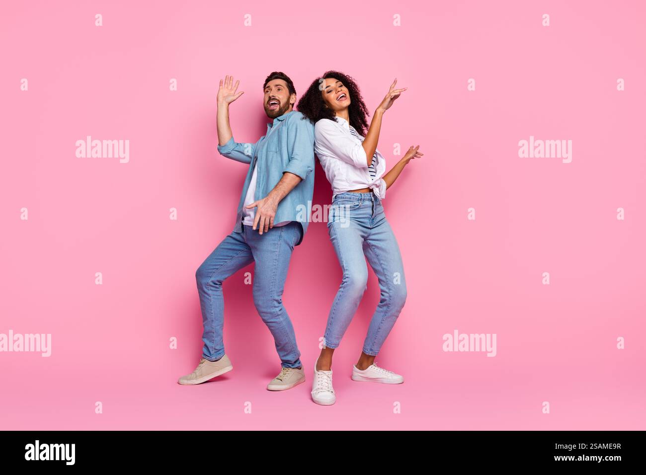 Couple posant de manière ludique sur fond rose dans des tenues décontractées en denim Banque D'Images