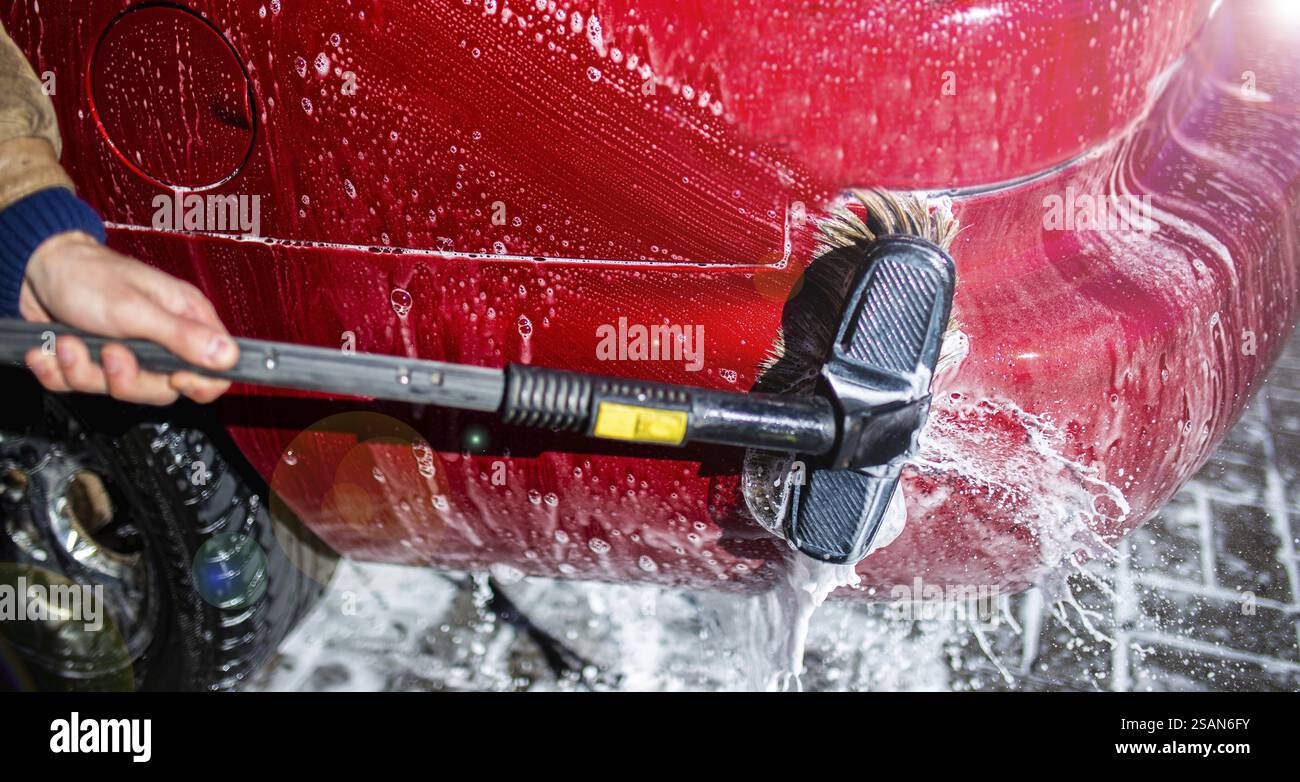 Une main nettoyant une voiture rouge avec une brosse et de l'eau savonneuse Banque D'Images