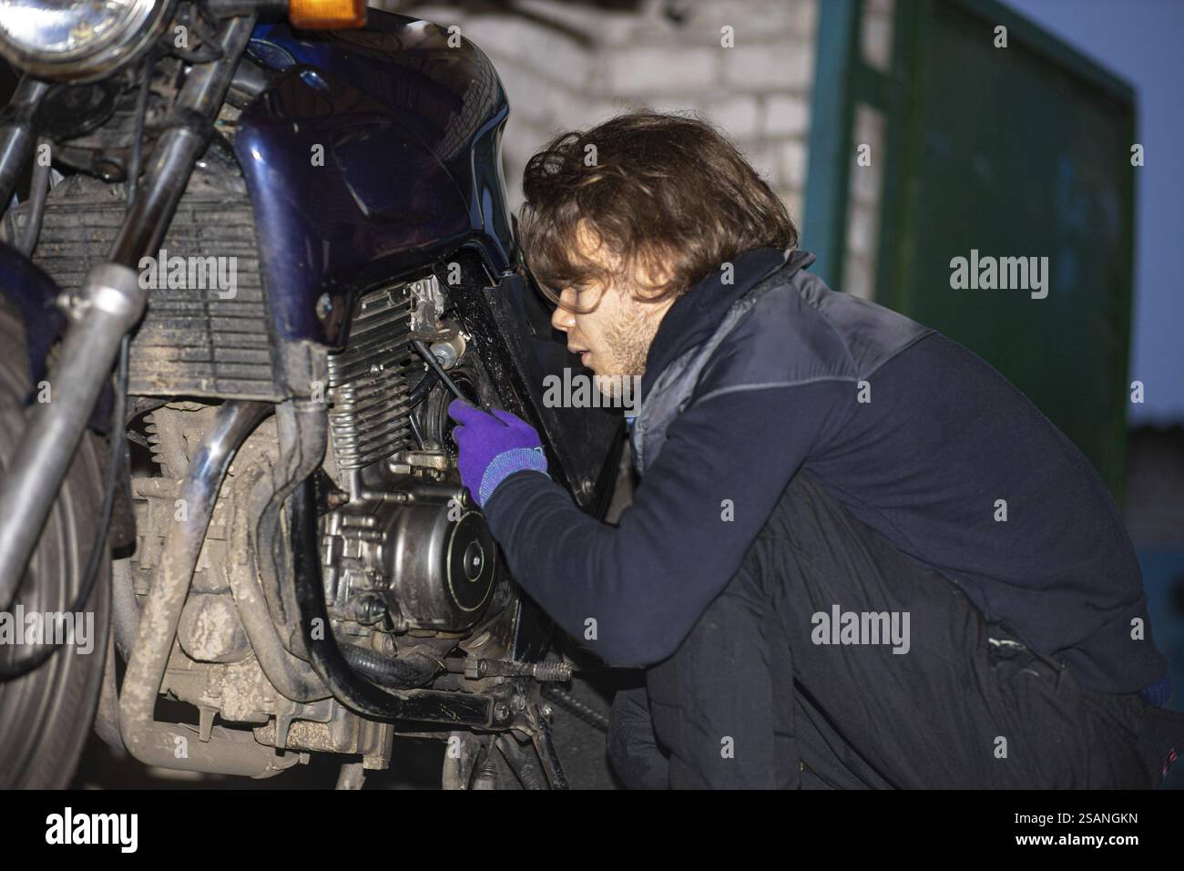 Personne répare une moto à l'intérieur, portant des gants, concentré sur la tâche Banque D'Images