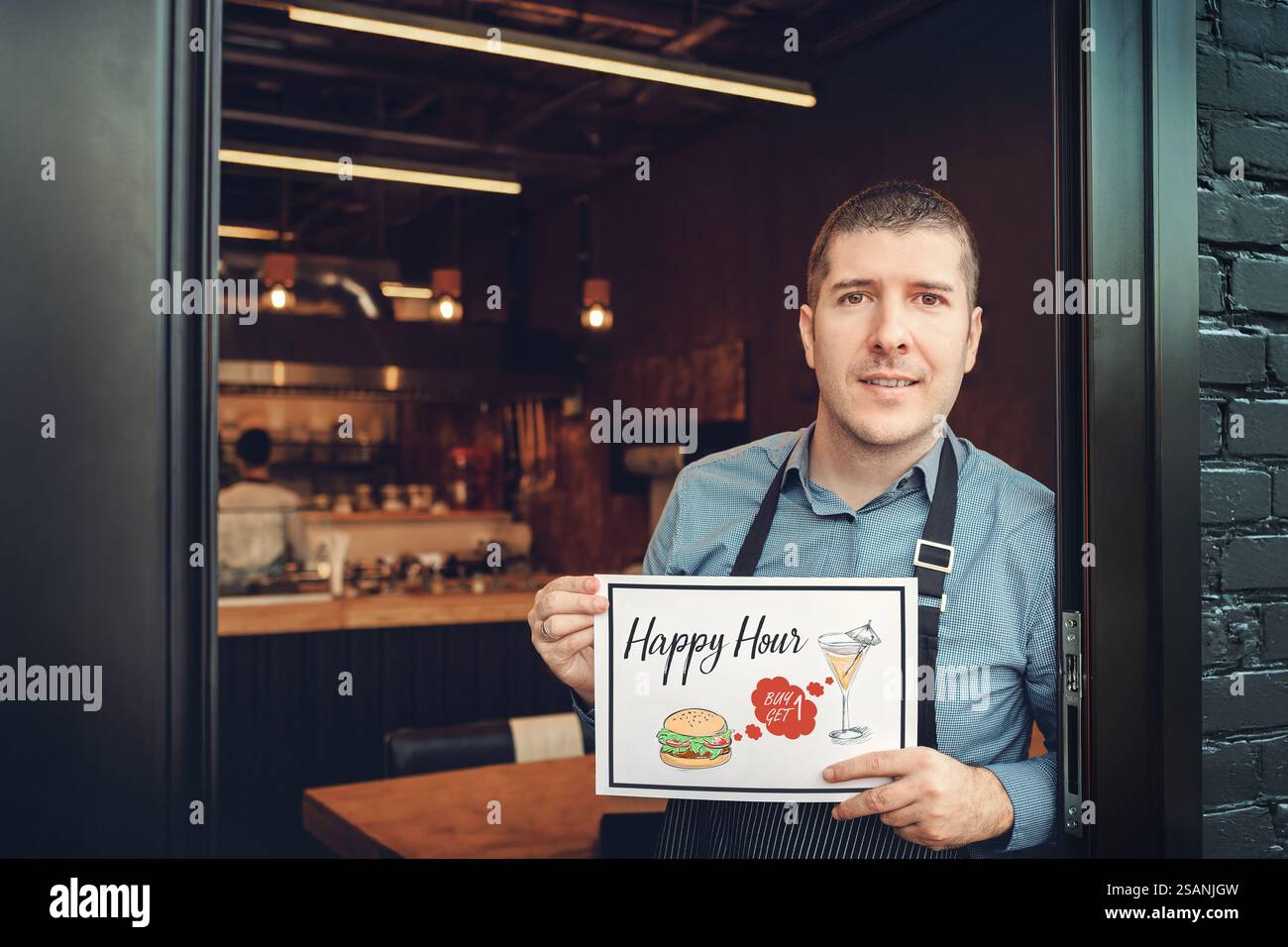 Heureux propriétaire d'entreprise à l'entrée du nouveau petit restaurant familial tenant un panneau Happy Hour faisant la promotion d'un menu de plats et de boissons Banque D'Images