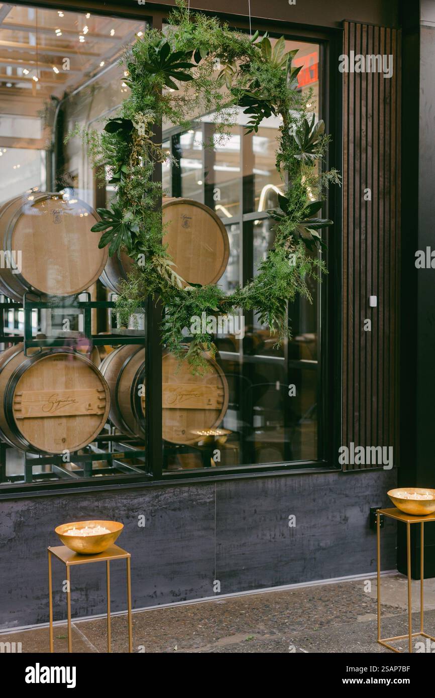 Un bel arrangement de verdure luxuriante encadre l'entrée d'un domaine viticole, mettant en évidence les tonneaux en bois à l'intérieur. Les accents dorés ajoutent une touche d'élégance à Banque D'Images