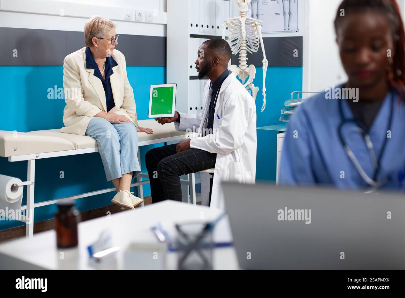 Médecin tenant un comprimé avec écran vert explique les plans de traitement de santé au patient senior alors que l'infirmière travaille à proximité. Médecin utilisant un appareil numérique avec maquette au cours d'une consultation de personnes âgées. Banque D'Images