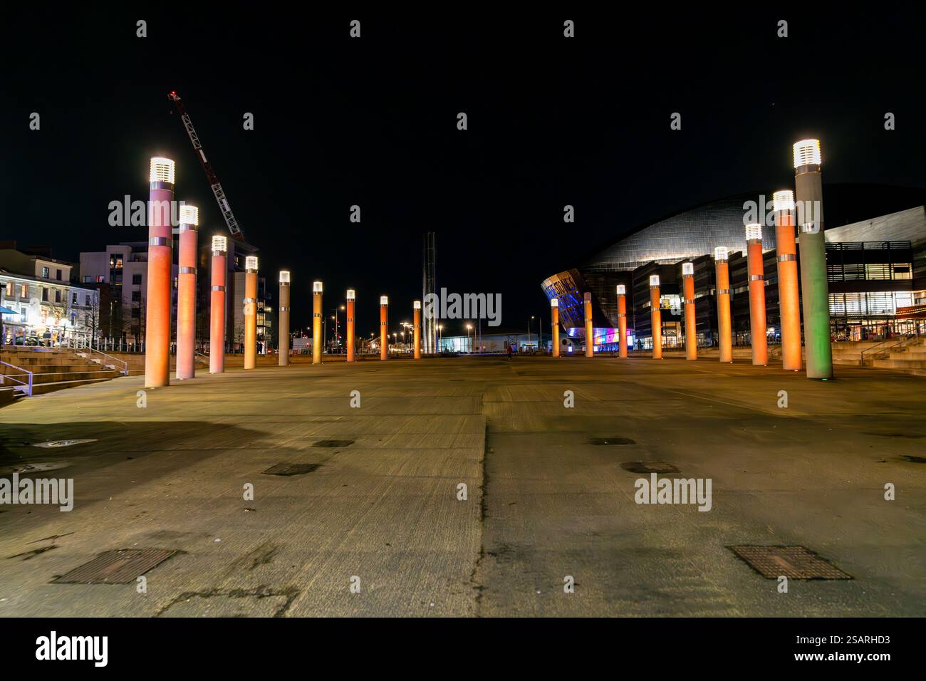 Roald Dahl Plass avec des piliers colorés illuminés dans le centre-ville de Cardiff la nuit avec Wales Millennium Centre en arrière-plan Banque D'Images