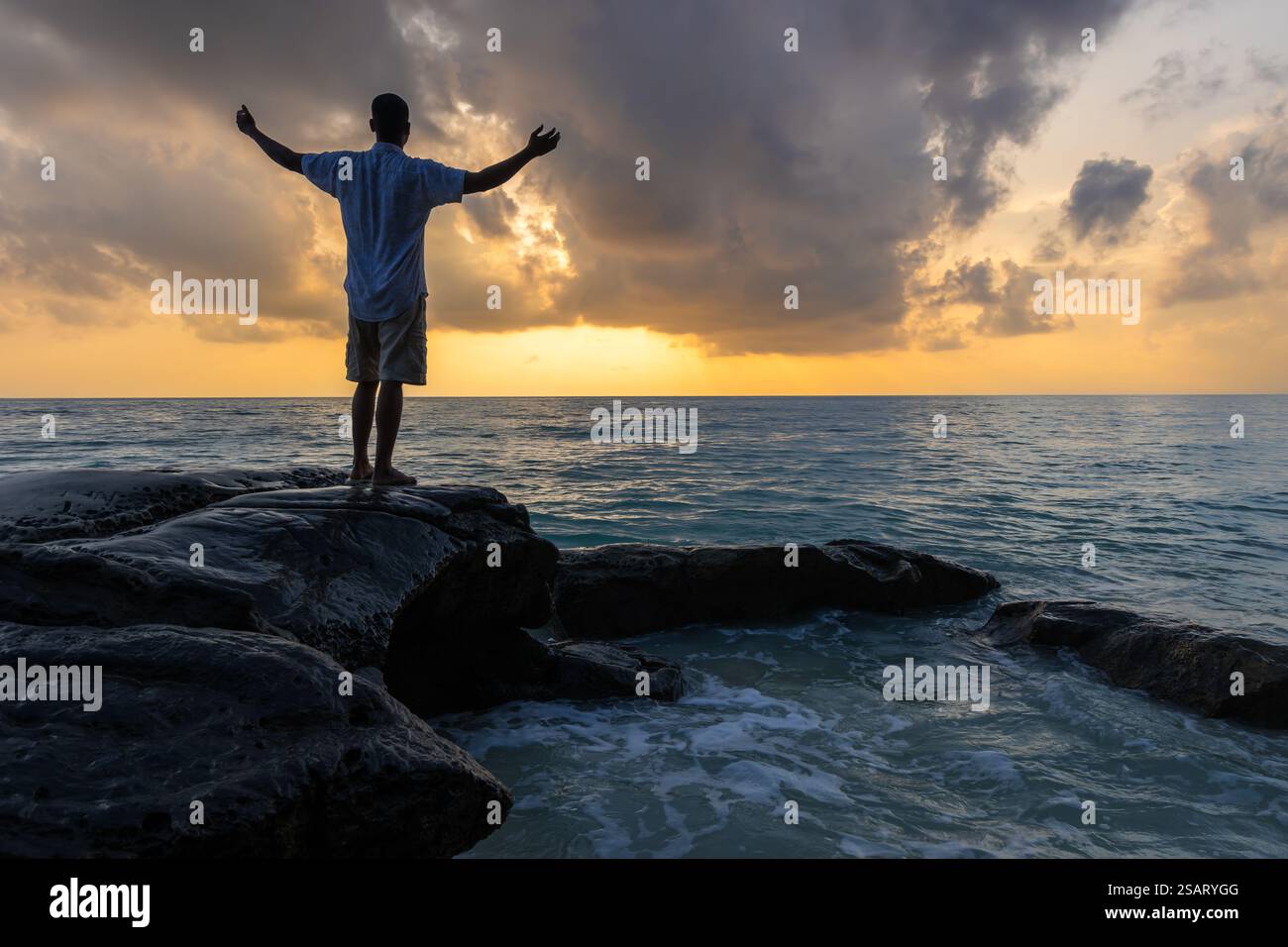 Jeune homme isolé avec les bras ouverts à la rive rocheuse et regardant l'horizon de la mer avec l'image spectaculaire du ciel est pris à Kala Pathar Beach havelock Andaman et Banque D'Images