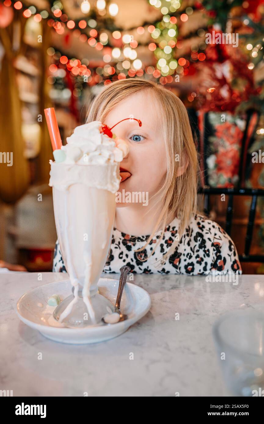 Une fille souriante profite d'un milk-shake festif dans un café décoré. Banque D'Images
