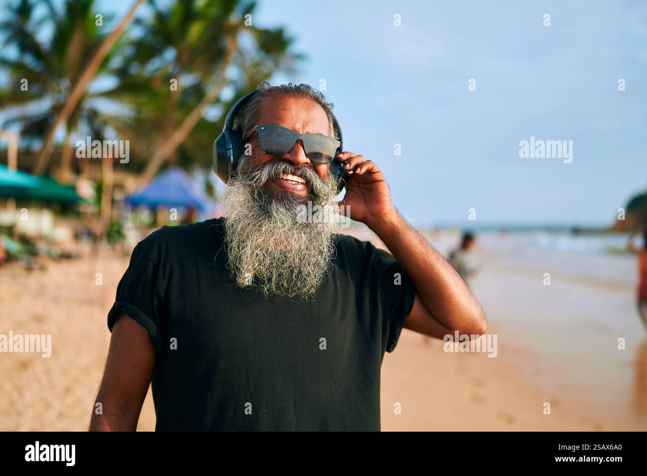 Homme âgé barbu grise, lunettes de soleil, écoute de la musique avec des écouteurs à la plage ensoleillée. Grand-père élégant aime les airs, se sentant jeune et dynamique Banque D'Images