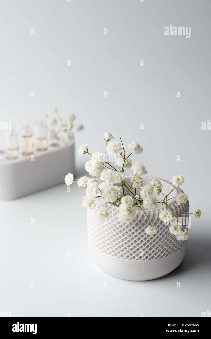 Une petite plante artificielle aux feuilles vertes éclatantes se trouve dans un pot blanc texturé sur un fond blanc propre Banque D'Images