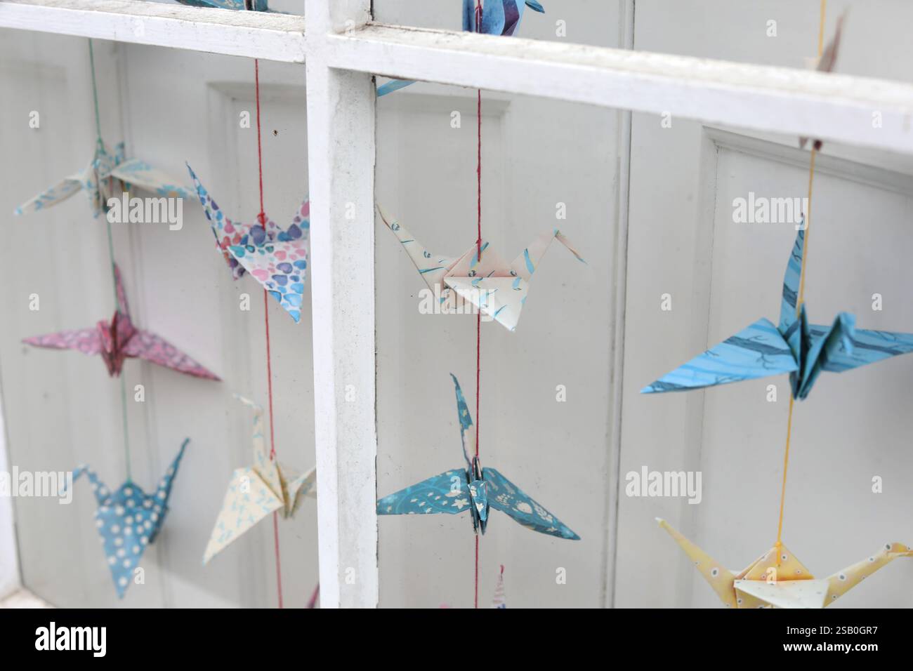 Une sélection de grues Orizuru, grues en origami ou grues en papier, un design classique japonais en origami, accroché dans une fenêtre à Chichester, West Sussex, Royaume-Uni. Banque D'Images