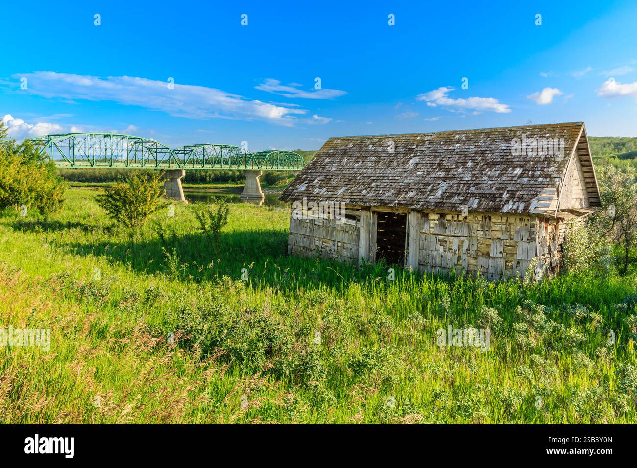 Une petite maison est dans un champ avec un pont en arrière-plan. La maison est en pierre et a un toit Banque D'Images