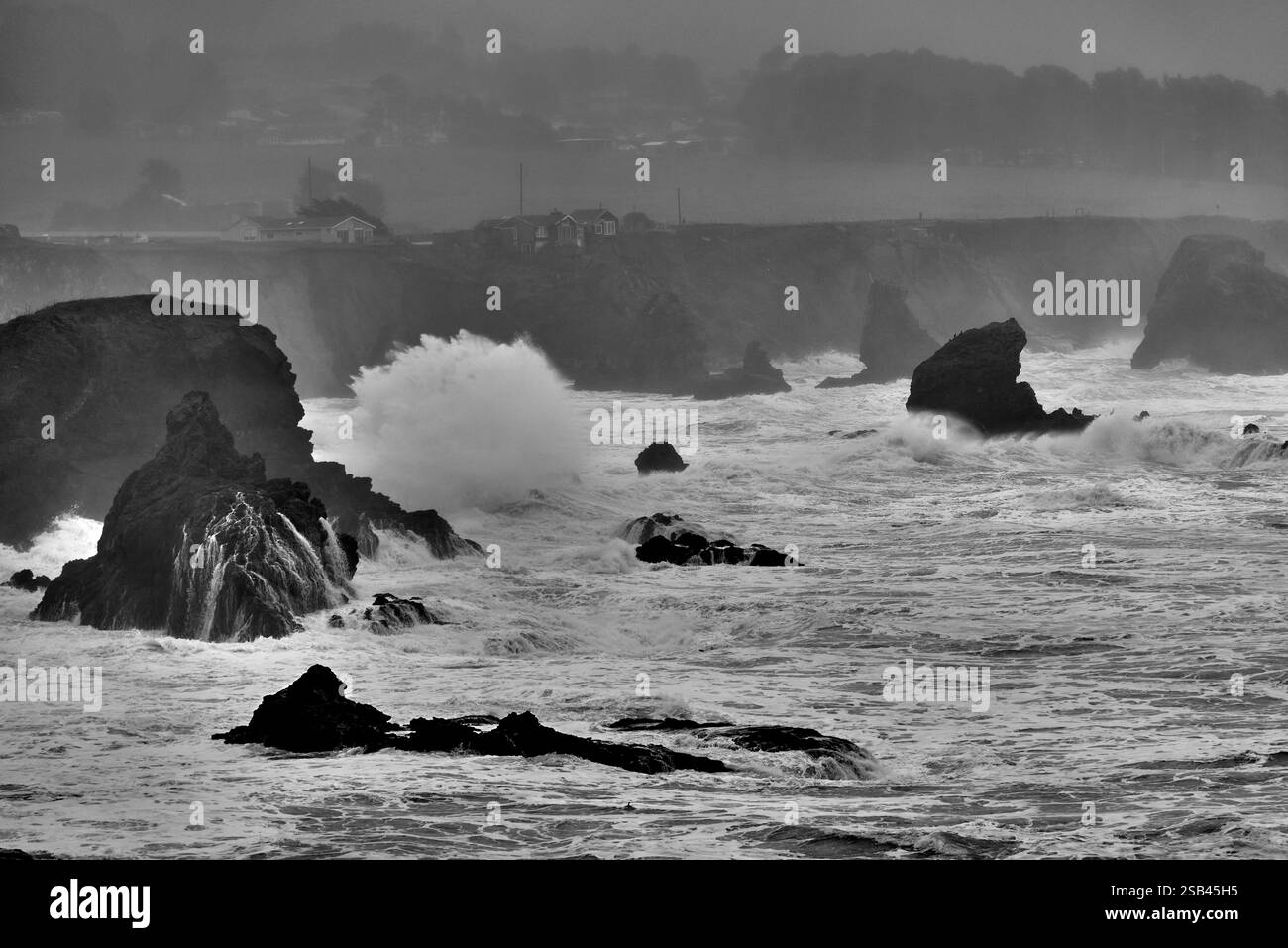 image en noir et blanc des vagues s'écrasant le long de la côte rocheuse pendant la tempête Banque D'Images