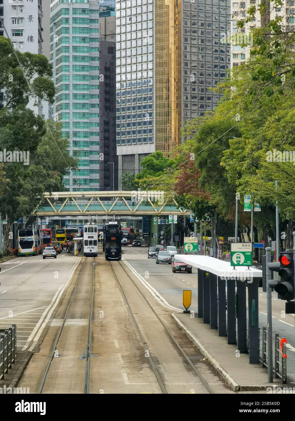 Hong Kong, Chine - 01 février 2025 : Un tramway de Hong Kong glisse le long de ses voies, flanqué de gratte-ciel modernes et de verdure luxuriante. Le paysage urbain Banque D'Images