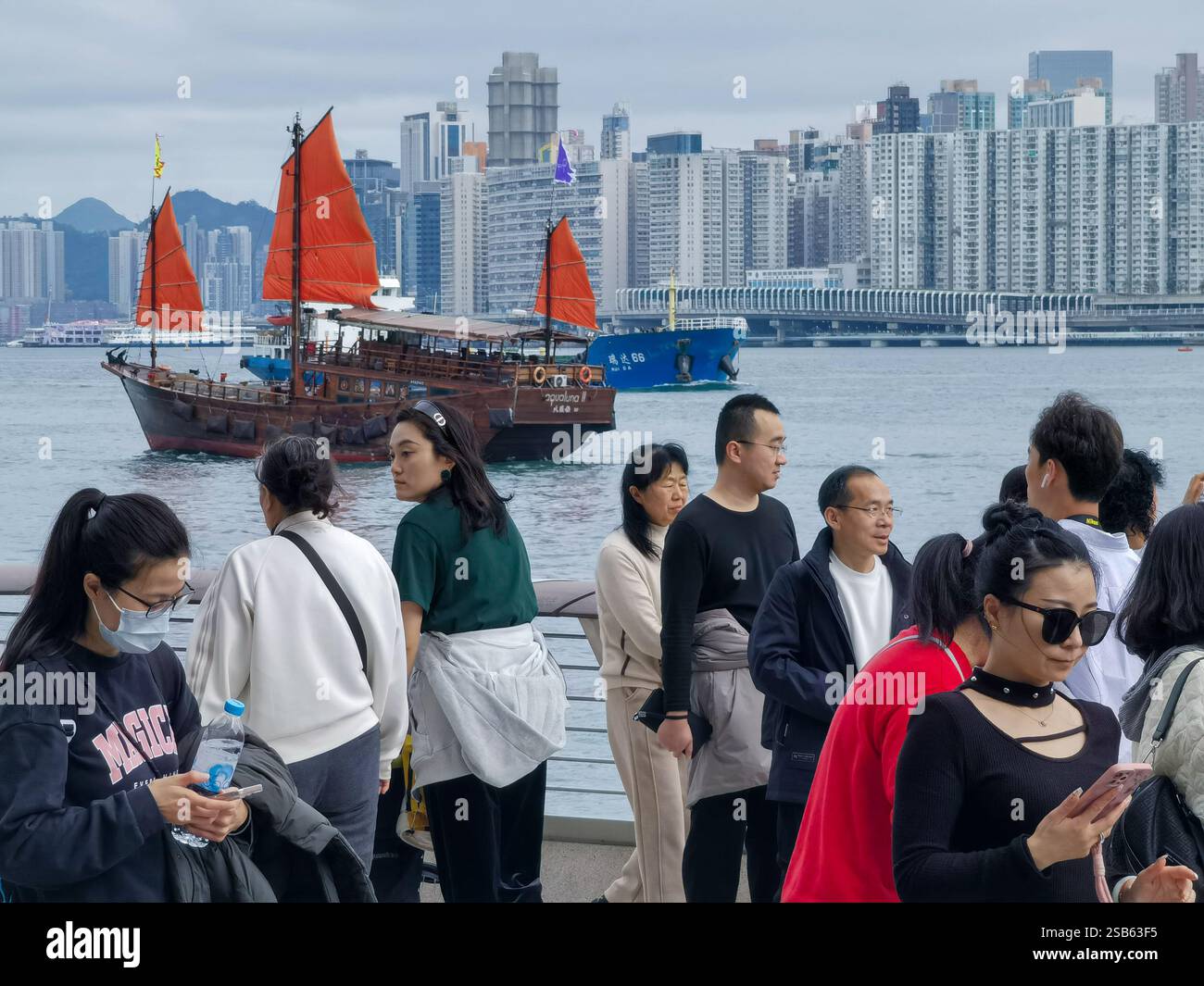 Hong Kong, Chine - 01 février 2025 : les touristes apprécient la promenade Tsim Sha Tsui pendant les vacances du nouvel an chinois. Une jonque traditionnelle navigue sur V. Banque D'Images