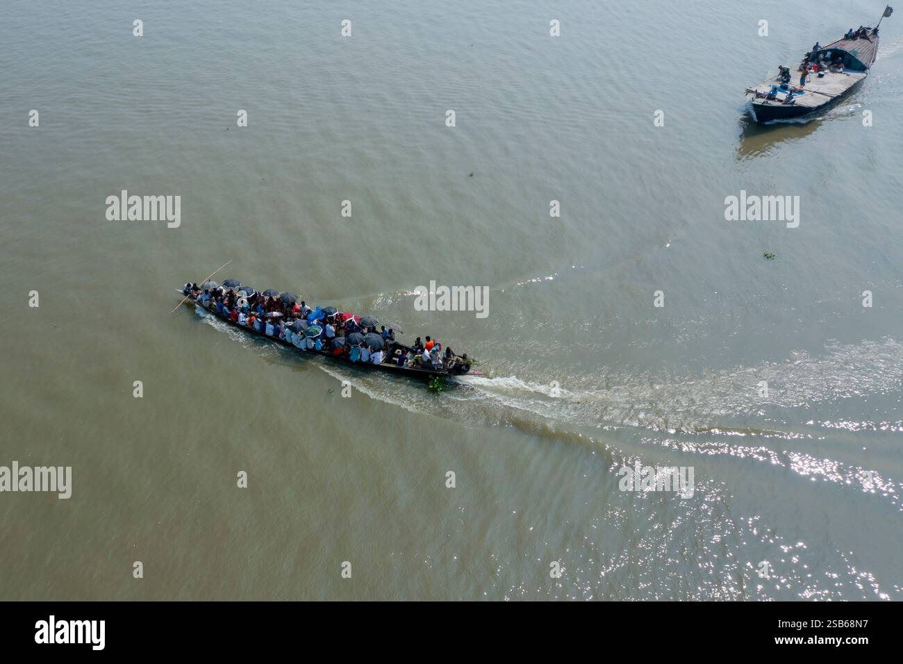Un bateau transportant des passagers, se protégeant avec des parapluies, flotte le long de la rivière Brahmapoutre à Bera, dans le district de Pabna, au Bangladesh. Banque D'Images