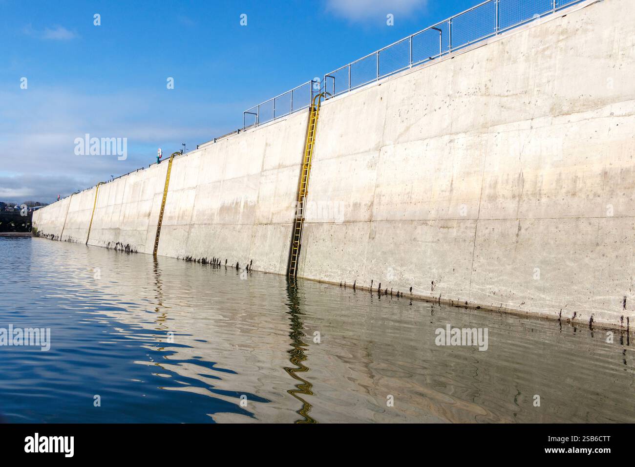 Structure de mur de port en béton avec une échelle en métal et des reflets dans l'eau calme sur une journée claire beadnell port northumberland royaume-uni Banque D'Images