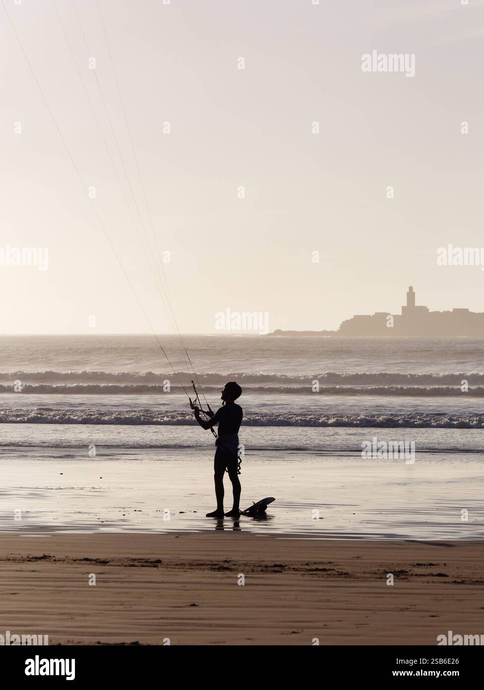 Kite surfeur se tient sur une plage de sable avec une île derrière dans la ville d'Essaouira, du 27 au 29 janvier 2025 Banque D'Images