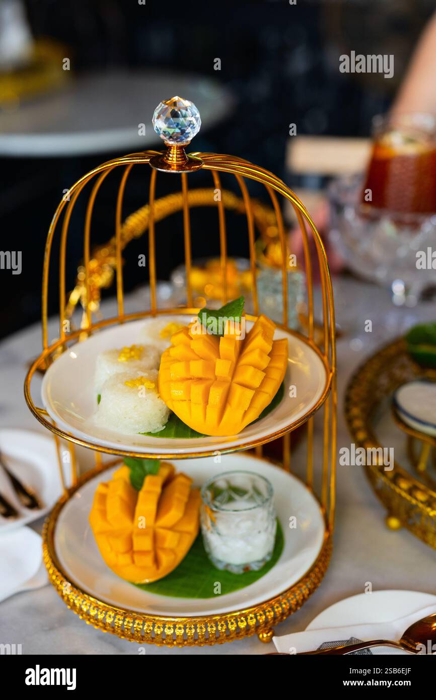 Une portion magnifiquement arrangée de riz collant à la mangue thaïlandaise avec des tranches de mangue fraîche, du riz gluant garni de haricots mungo et du lait de coco Banque D'Images
