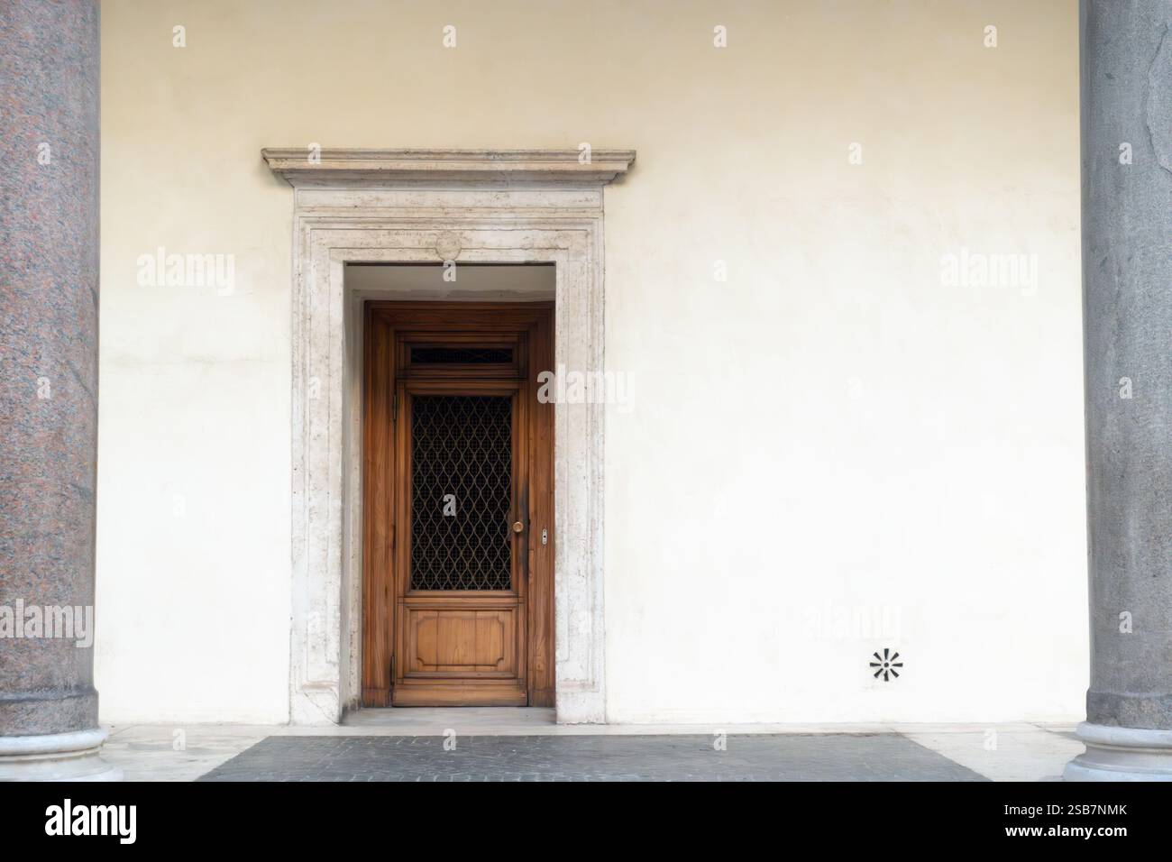 Vieille porte en bois sur un mur de plâtre blanc de bâtiment médiéval en pierre entre deux colonnes grises Banque D'Images