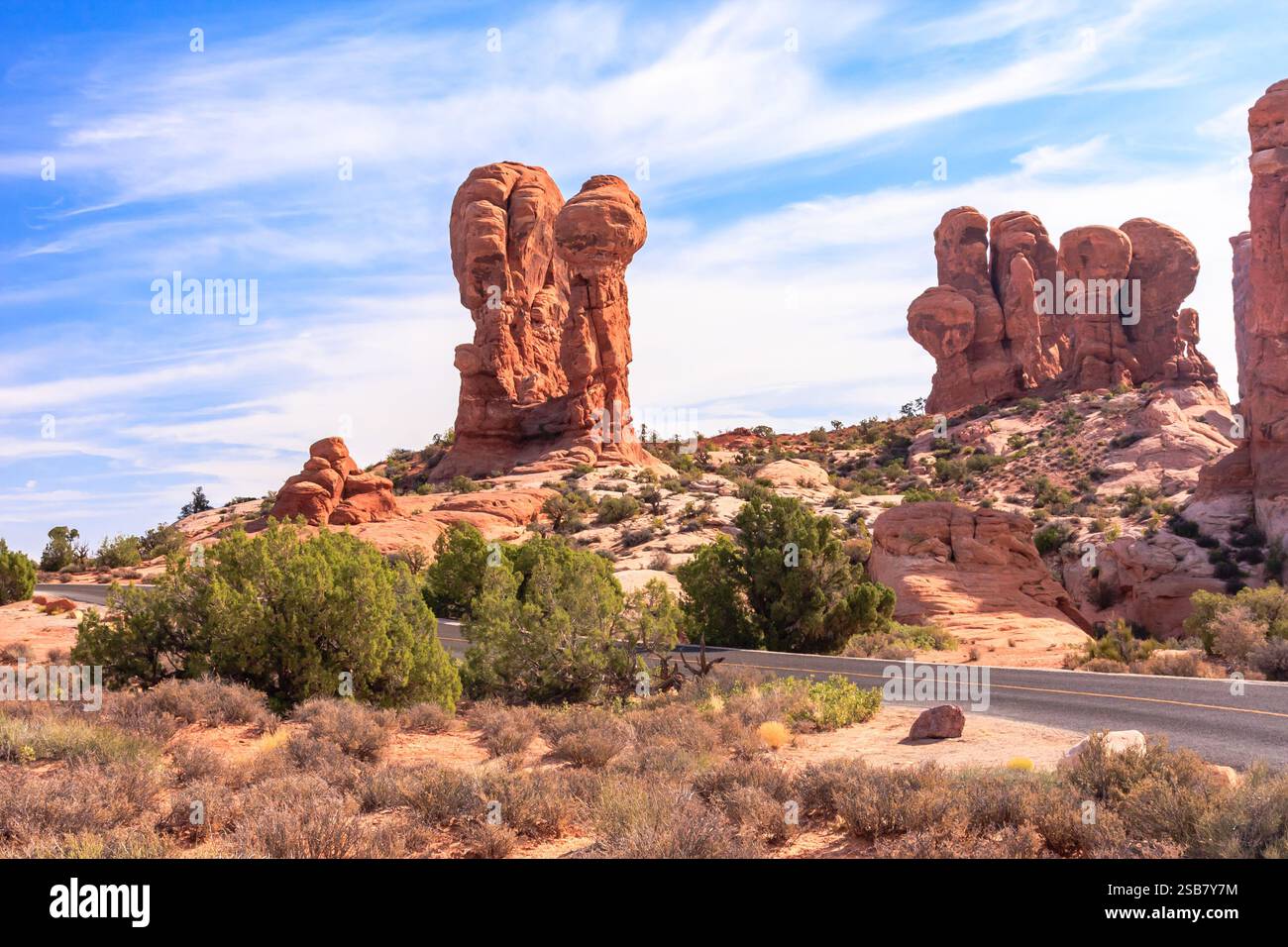 Un paysage désertique avec une route et quelques gros rochers. Le ciel est bleu et il y a quelques nuages Banque D'Images