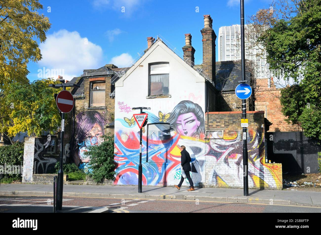 Un homme passe devant une toile de fond colorée de graffiti Street art sur le mur d'un bâtiment par les artistes Kaldea et Doudou style, Croydon, Angleterre, Royaume-Uni. Urbain Banque D'Images
