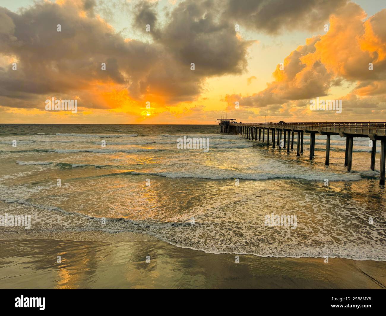 Coucher de soleil orange sur l'océan avec jetée, reflet dans le sable, mousse dans les vagues, côte ouest, USA, Amérique - Image de stock capturée avec un smartphone