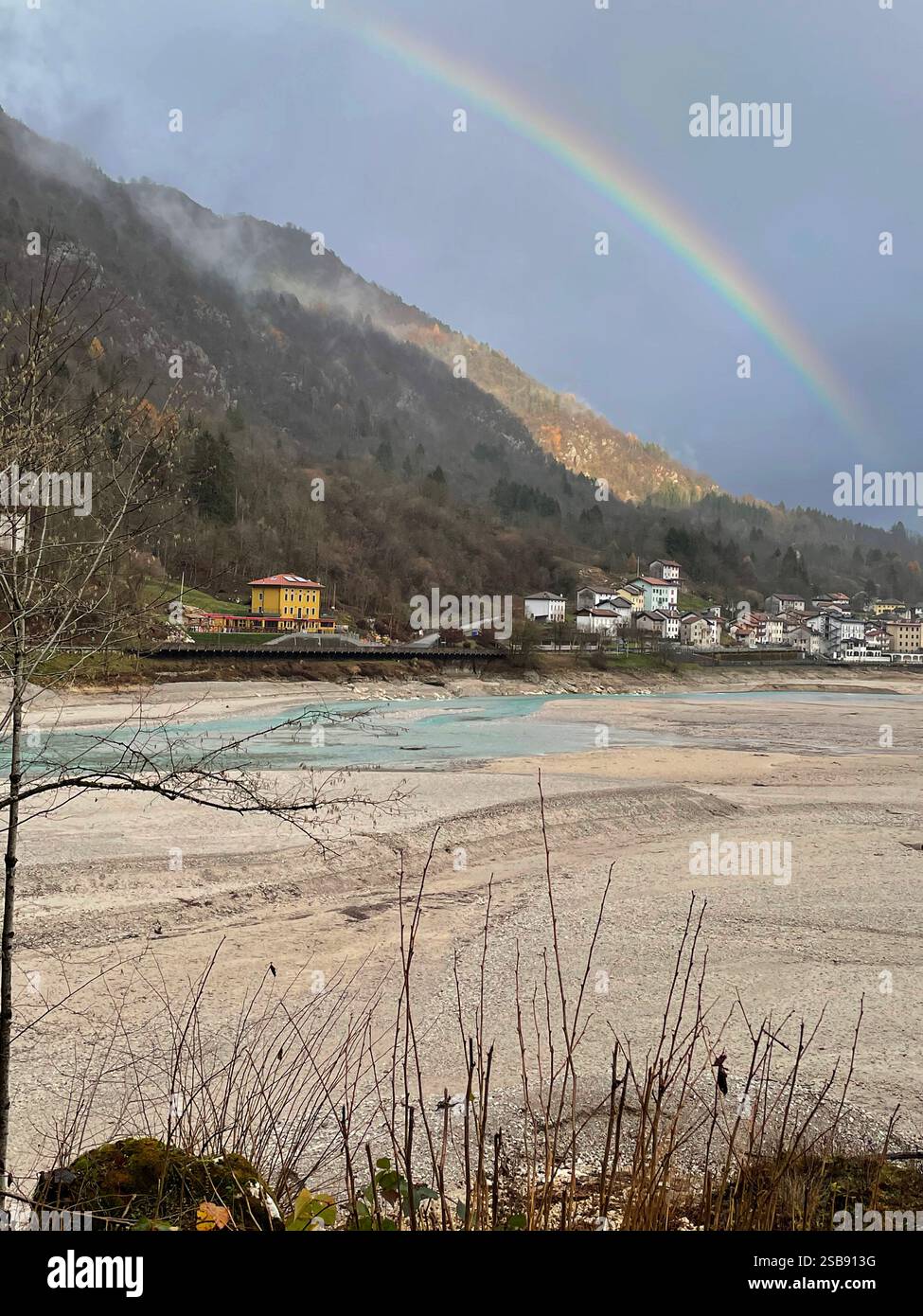 Barcis, Italie. Arc-en-ciel sur le lac Barcis, à moitié vidé en hiver, et les montagnes environnantes. - Image de stock capturée avec un smartphone