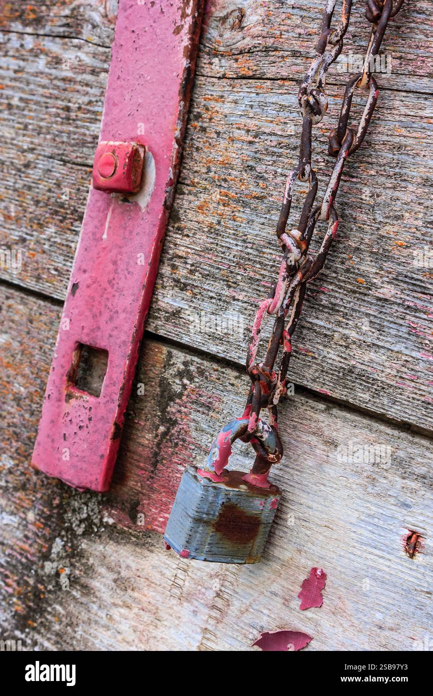 Une chaîne rouillée pend d'une serrure rouillée. La serrure est rouge et la chaîne est argentée Banque D'Images