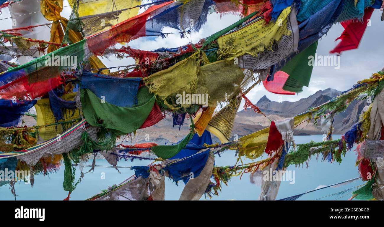 De vieux drapeaux de prière déchirés flottent dans le vent et la neige au-dessus du lac Tilicho. Banque D'Images