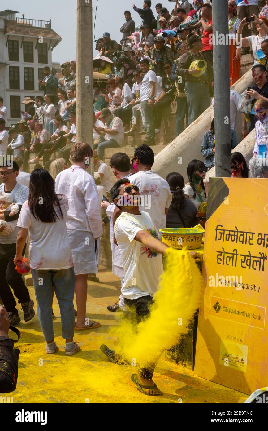 Un homme jette une couleur jaune avec une foule de gens derrière lui sur la place Durbar à Katmandou, au Népal. Banque D'Images