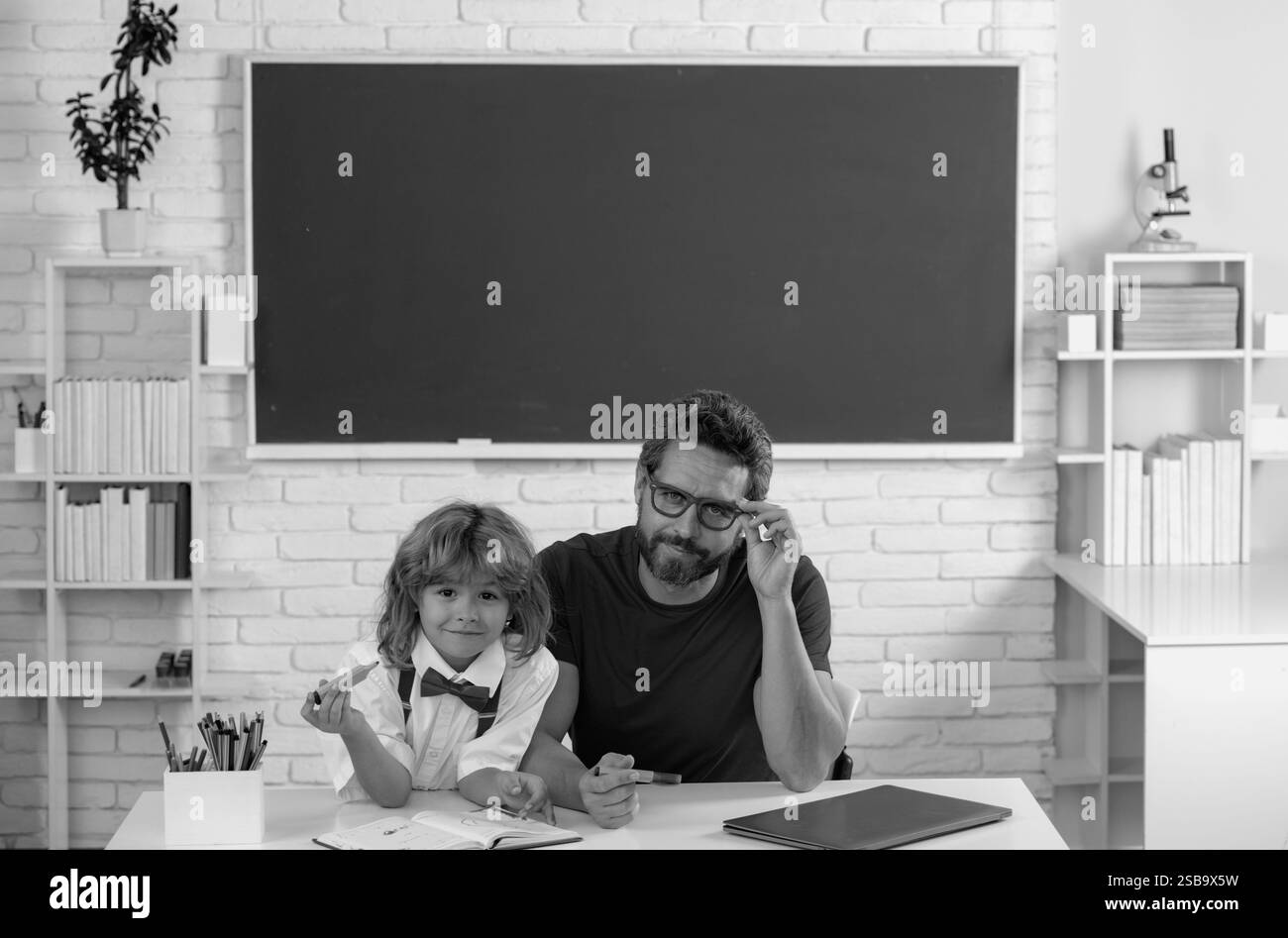 Garçon de l'école primaire en classe. Enseignant expliquant à l'élève. Professeur de père aidant un garçon de fils dans les cours d'école. Banque D'Images