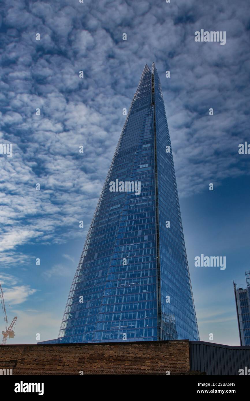 The Shard, un haut gratte-ciel en verre à Londres, est bien en vue contre un ciel nuageux. Un mur de briques et une partie d'un autre bâtiment sont visib Banque D'Images
