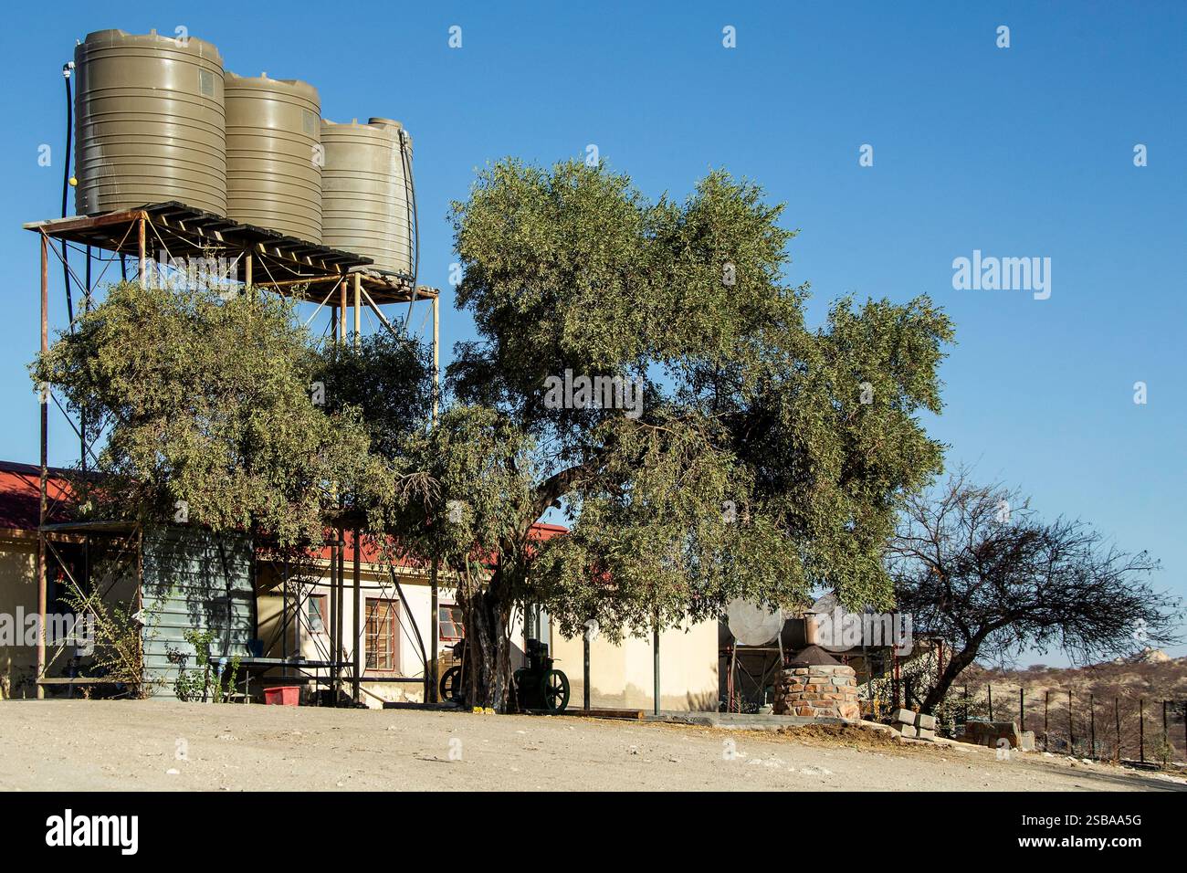 Trois réservoirs d'eau en plastique soulevés sur une structure en acier à côté d'une ferme namibienne au toit rouge. Banque D'Images