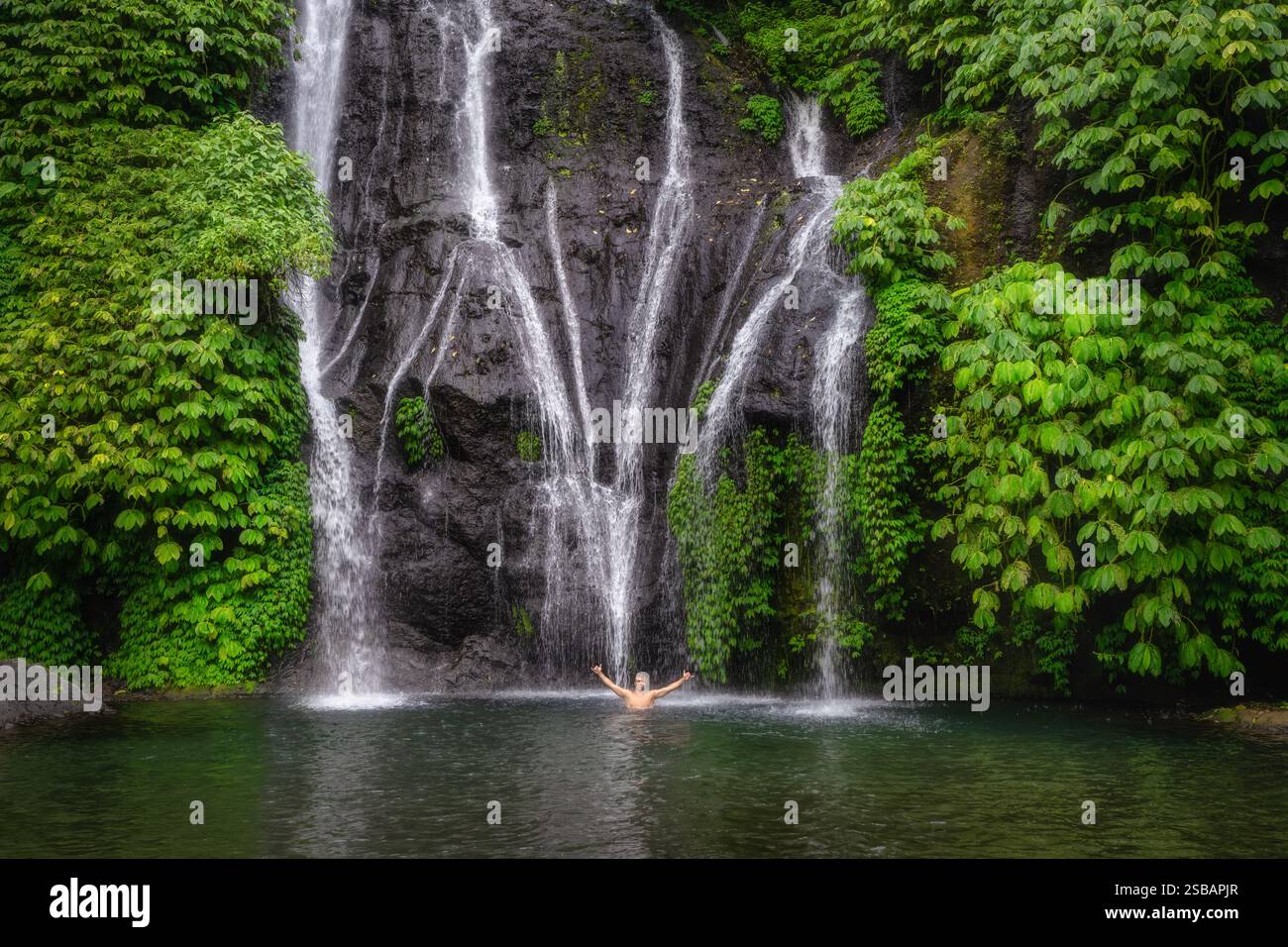 Un homme apprécie les superbes cascades de Banyumala Twin qui cascades dans la piscine claire entourée de verdure vibrante et de plantes tropicales créant un enchantin Banque D'Images