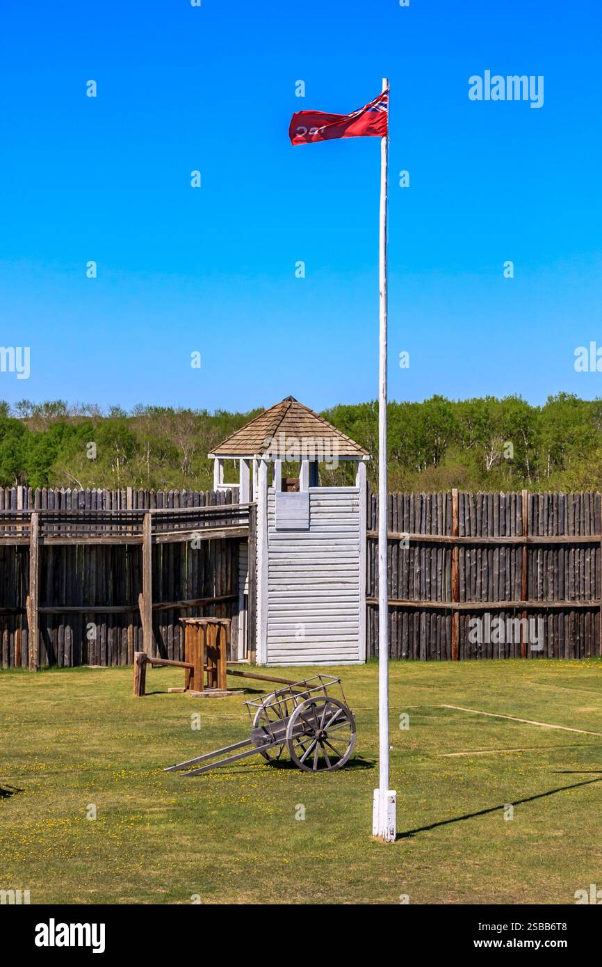 Un mât de drapeau avec un drapeau rouge volant dans les airs. Le drapeau est sur un poteau devant un bâtiment en bois Banque D'Images