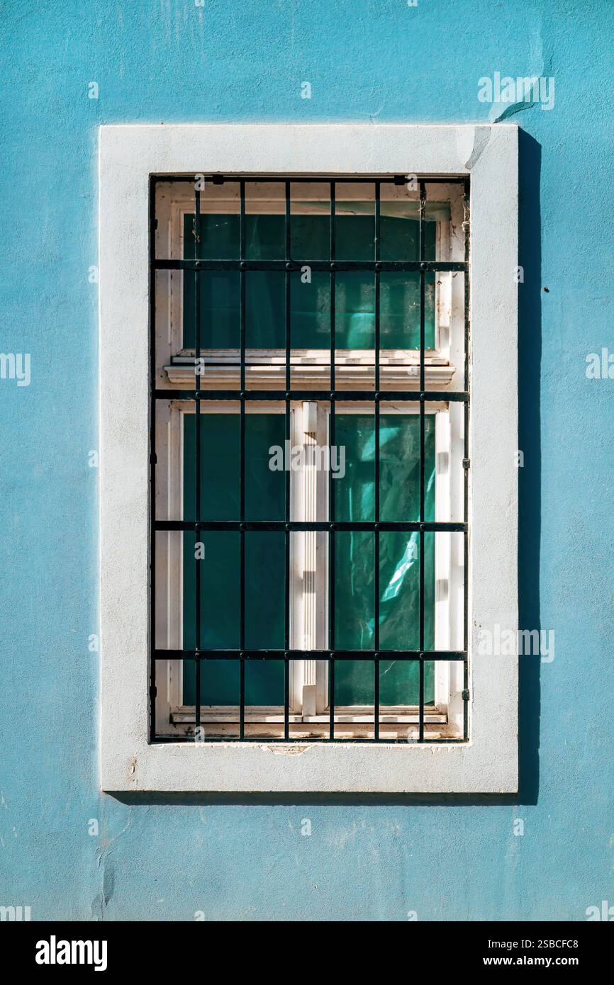 Vieille fenêtre avec cage de barres métalliques de protection et cadre en béton blanc sur un mur bleu, image verticale Banque D'Images Vieille fenêtre avec cage de barres métalliques de protection et cadre en béton blanc sur un mur bleu, image verticale Banque D'Images