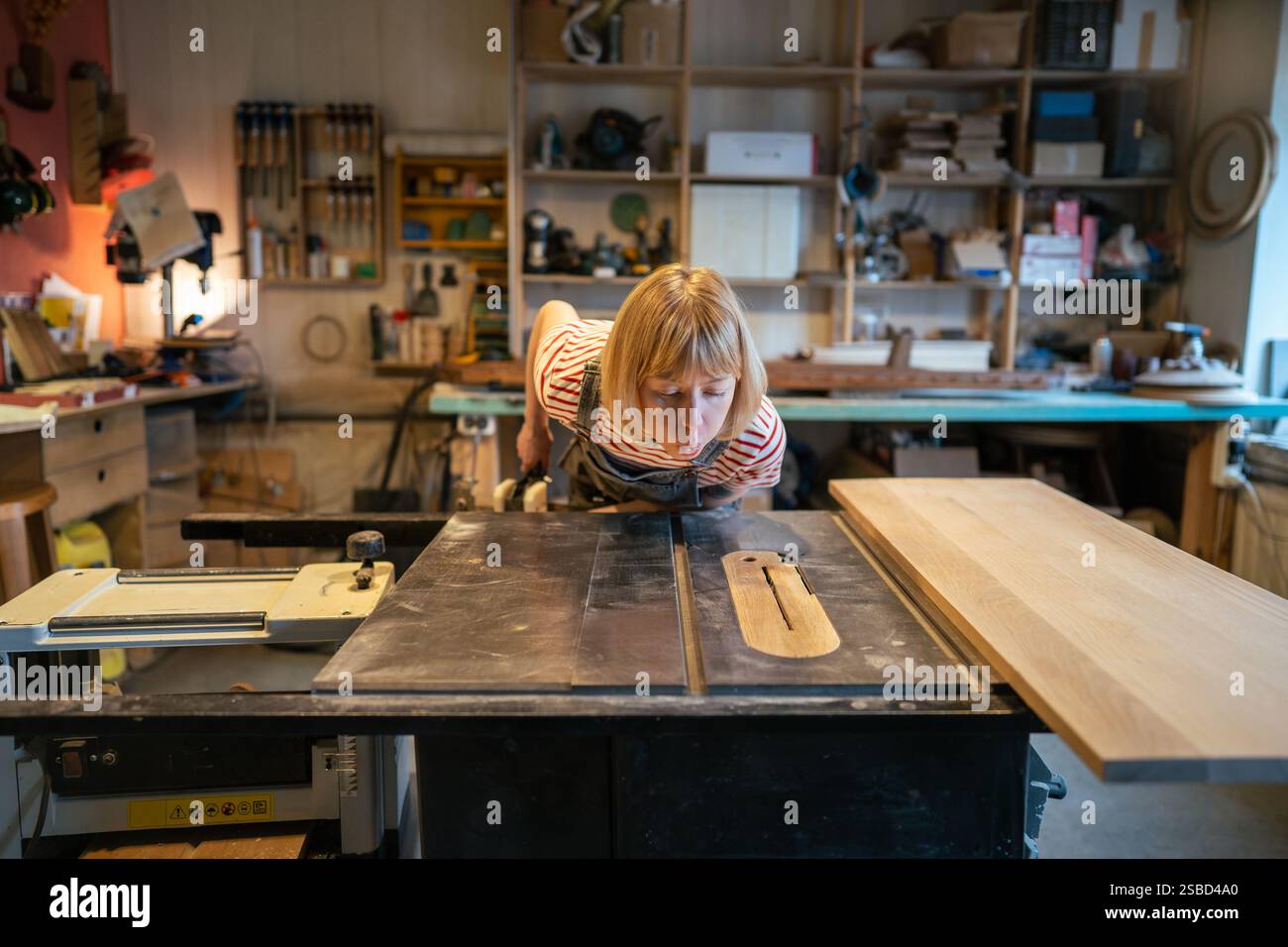 Femme à tout faire soufflant la poussière hors de la surface de la table avant de commencer le travail de scie circulaire dans l'atelier Banque D'Images