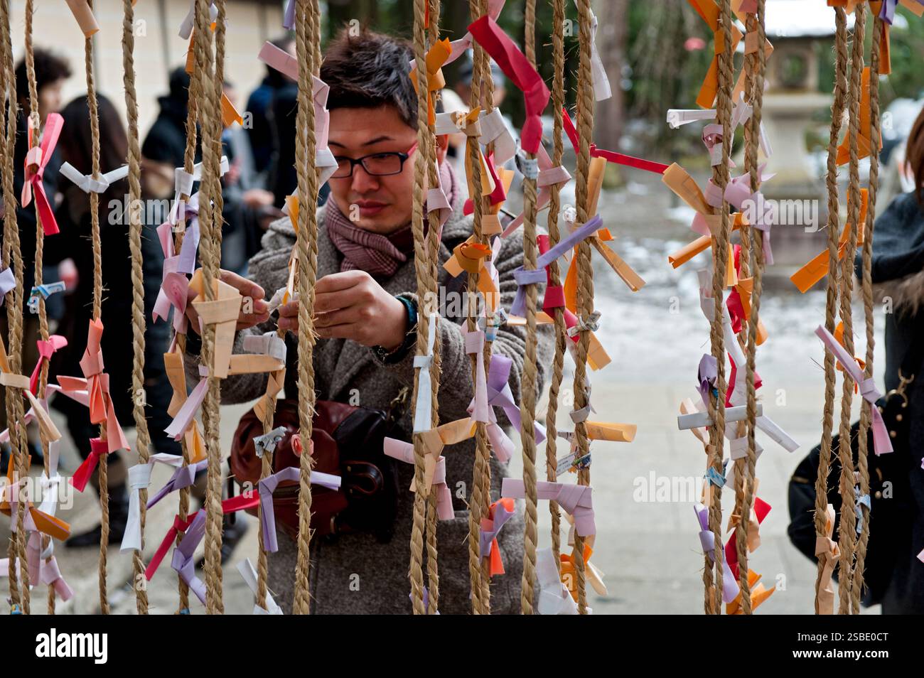 Homme attachant un 'omikuji' (oracle papier bonne ou mauvaise chance) à une corde pendant 'hatsumode' (visite du sanctuaire du nouvel an) à Taga Taisha, Hikone, Japon. Banque D'Images