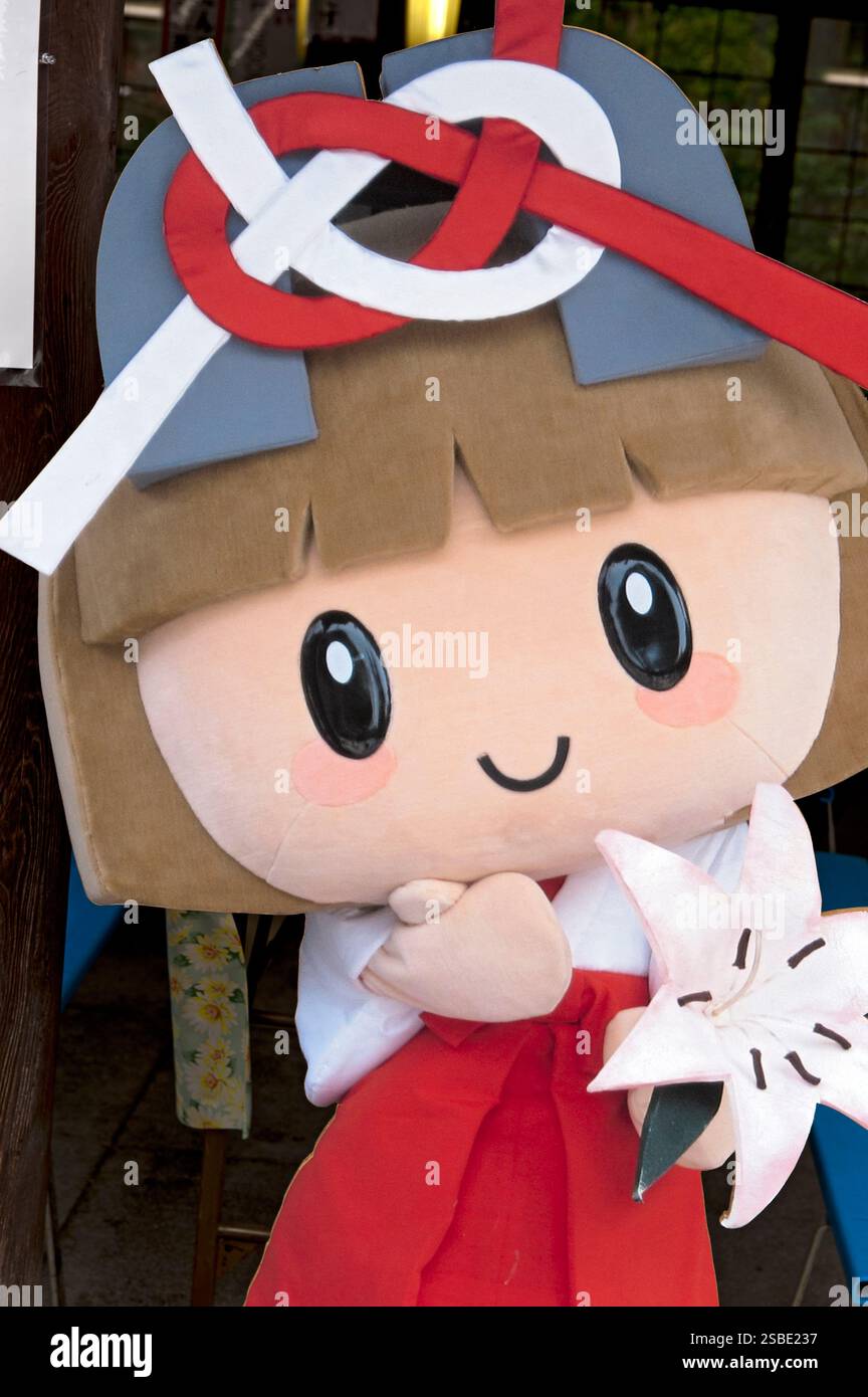 Sanctuaire Taga Taisha Shinto Yuru-kyara mascotte Tagayui-chan avec un noeud Awaji rouge et blanc 'mizuhiki' sur son chapeau portant un lis blanc, Hikone, Japon. Banque D'Images