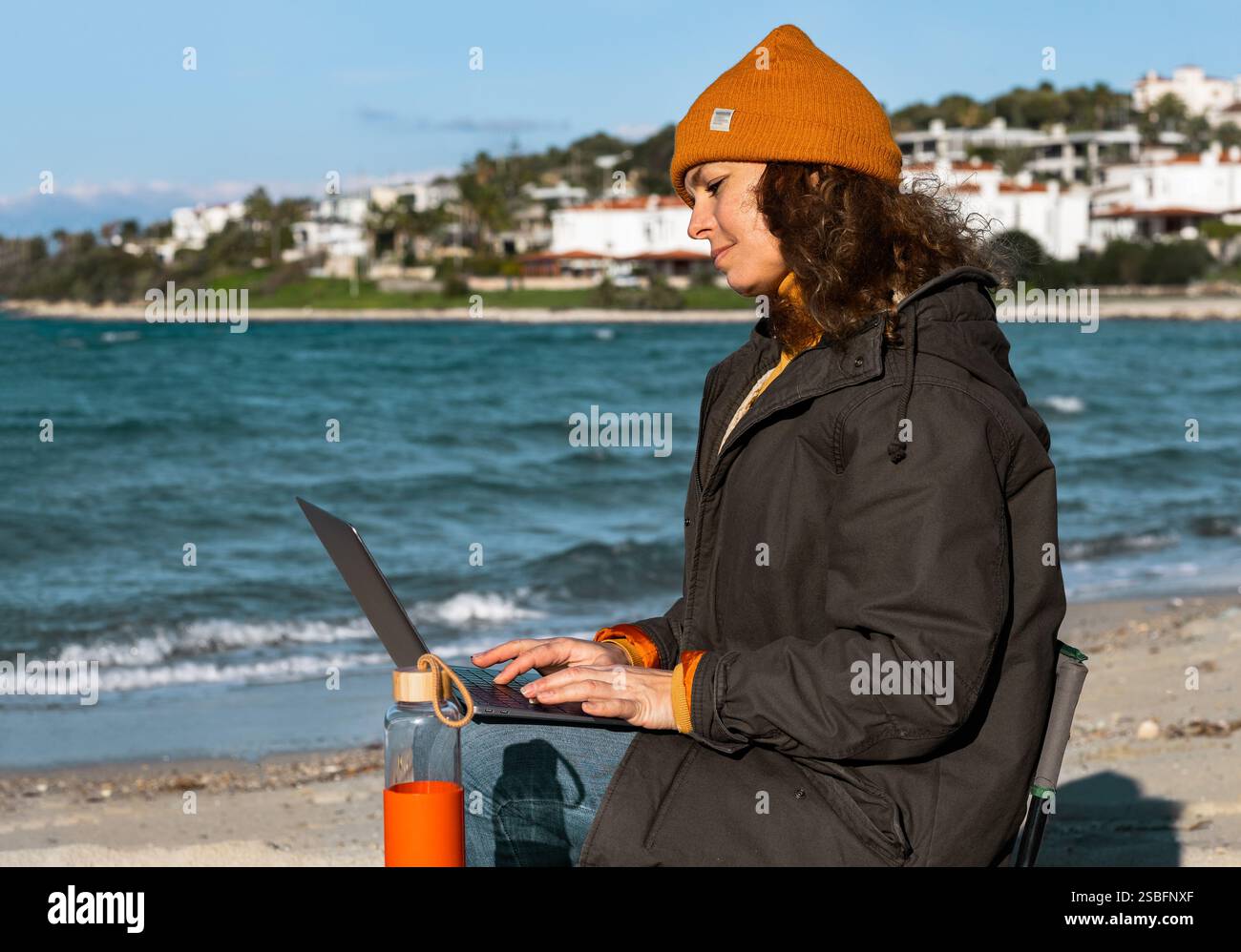 Jeune femme utilisant un ordinateur portable par la mer dans des vêtements d'hiver Banque D'Images