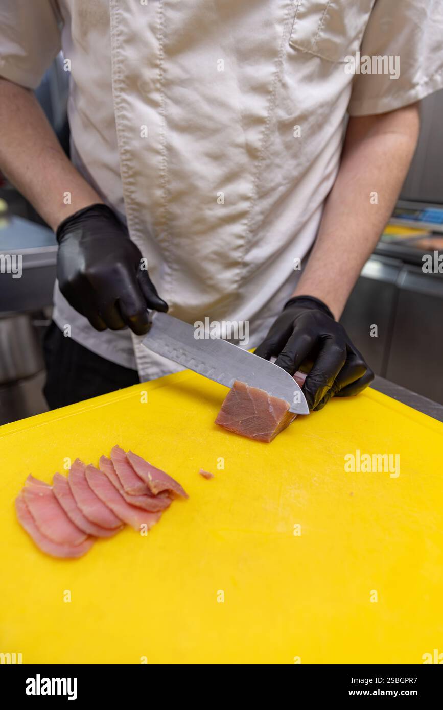 Chef tranchant du thon frais, préparant un délicieux repas dans une cuisine professionnelle Banque D'Images