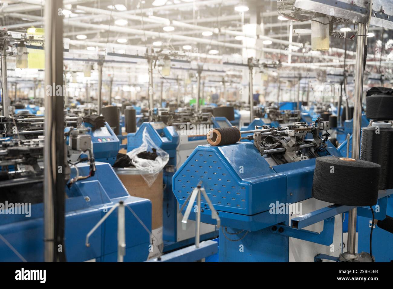 Vue de machines automatisées de fabrication de textiles dans une usine, avec des bobines de fil blanc prêtes pour le traitement. Banque D'Images