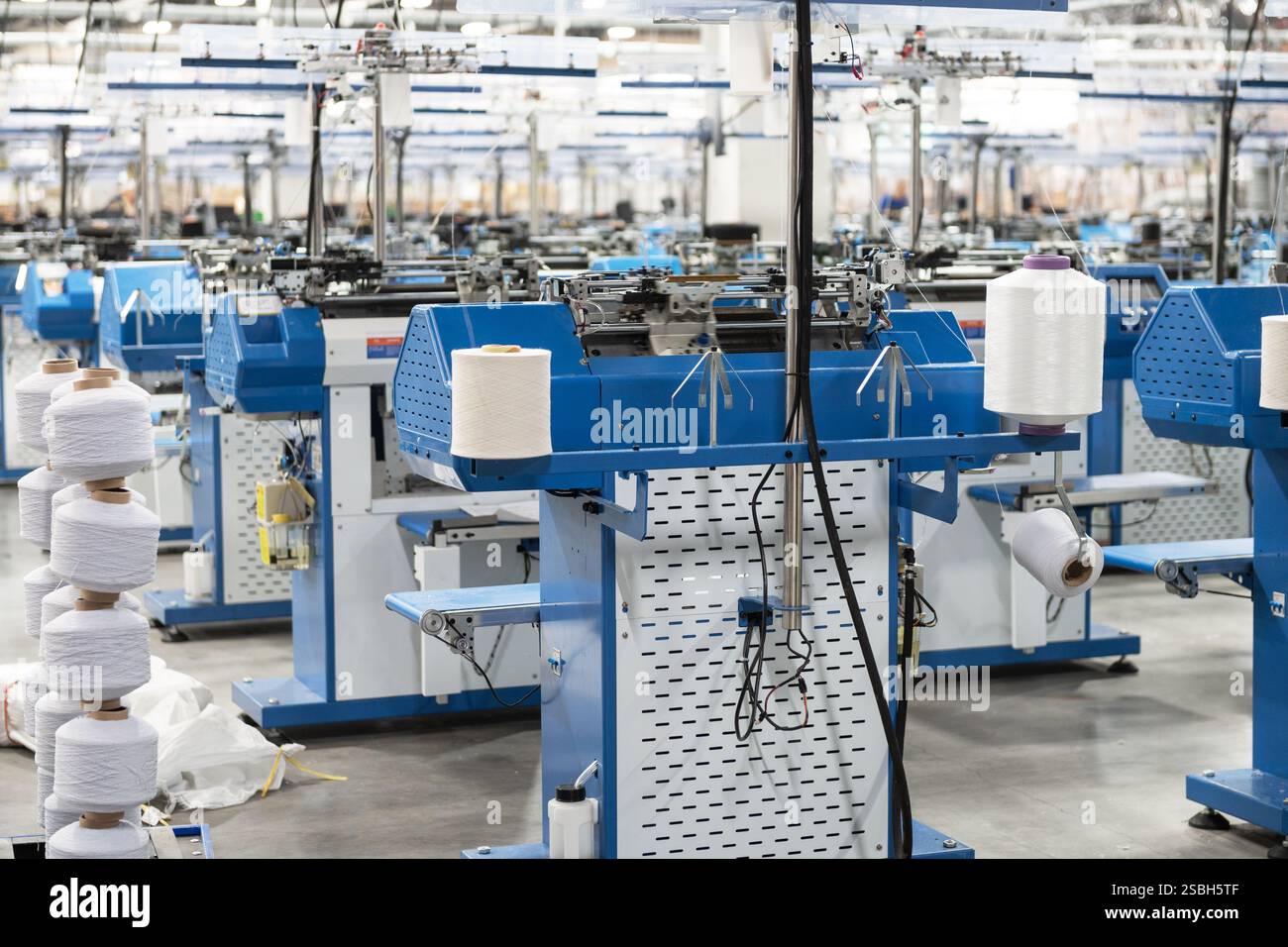 Vue de machines automatisées de fabrication de textiles dans une usine, avec des bobines de fil blanc prêtes pour le traitement. Banque D'Images
